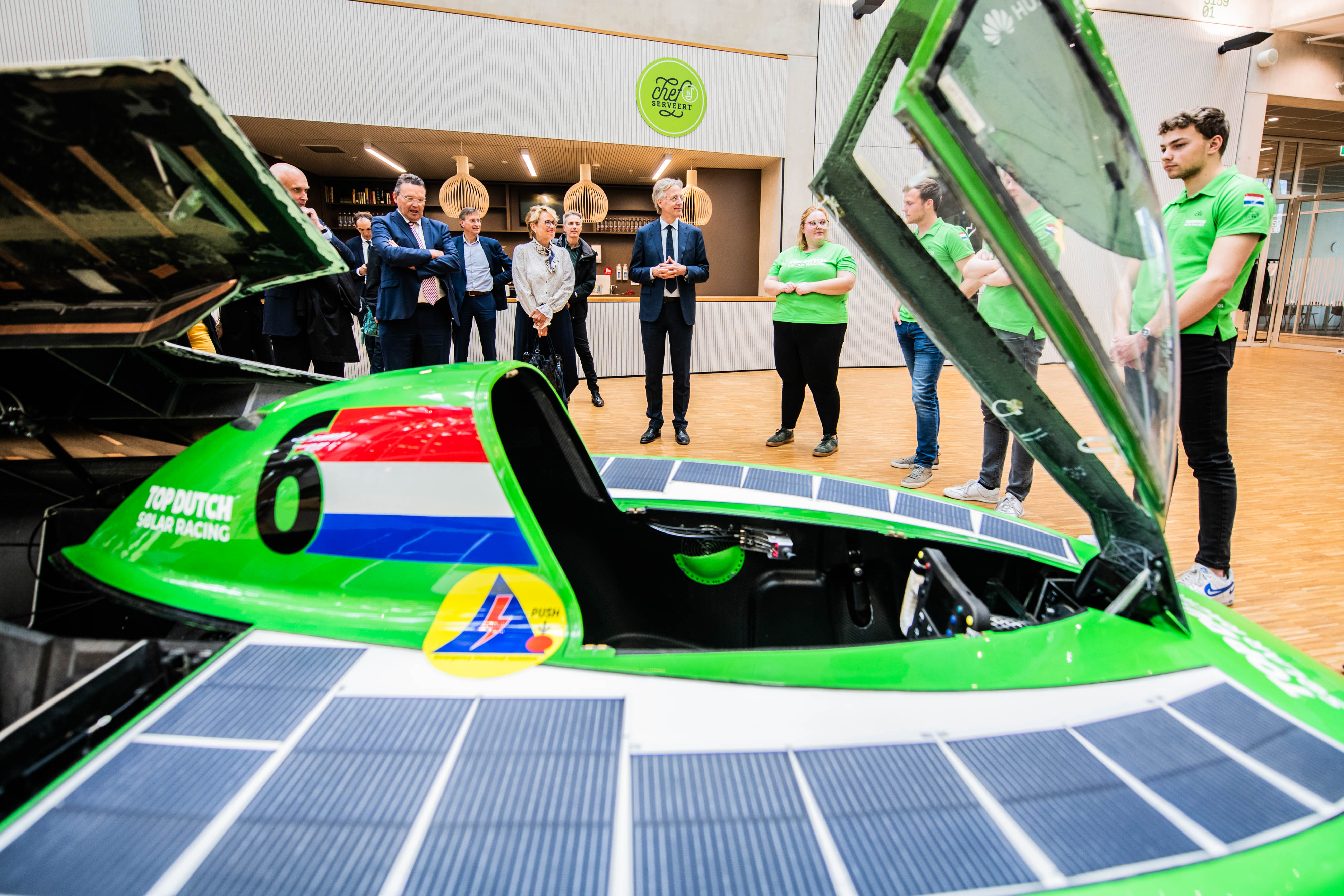 Groep mensen bekijkt een zonneauto tijdens een demonstratie gericht op duurzaam onderwijs en techniek.