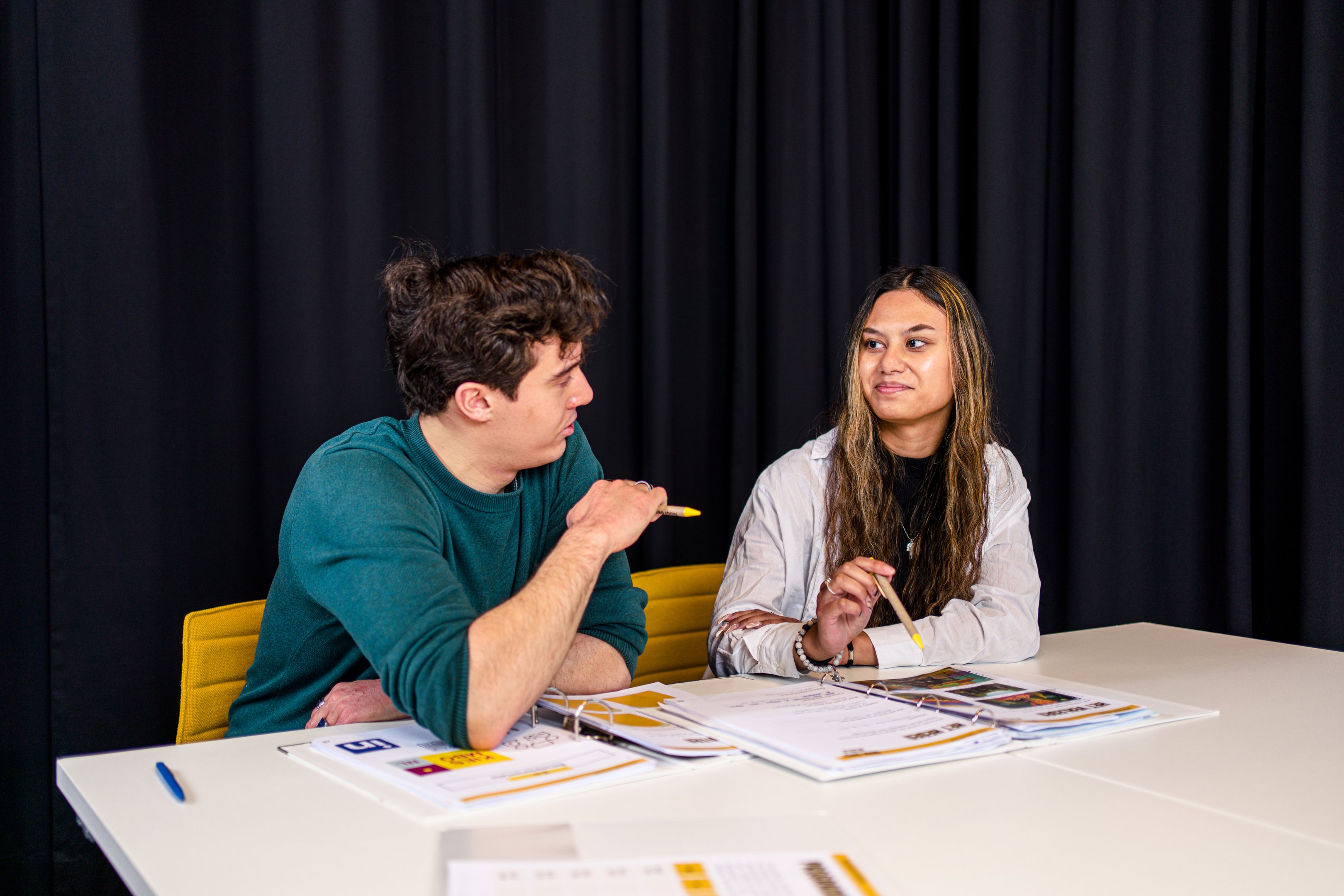 Twee mbo-studenten in gesprek tijdens een studieopdracht aan tafel met boeken en werkbladen
