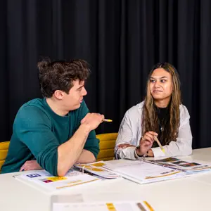Twee mbo-studenten in gesprek tijdens een studieopdracht aan tafel met boeken en werkbladen