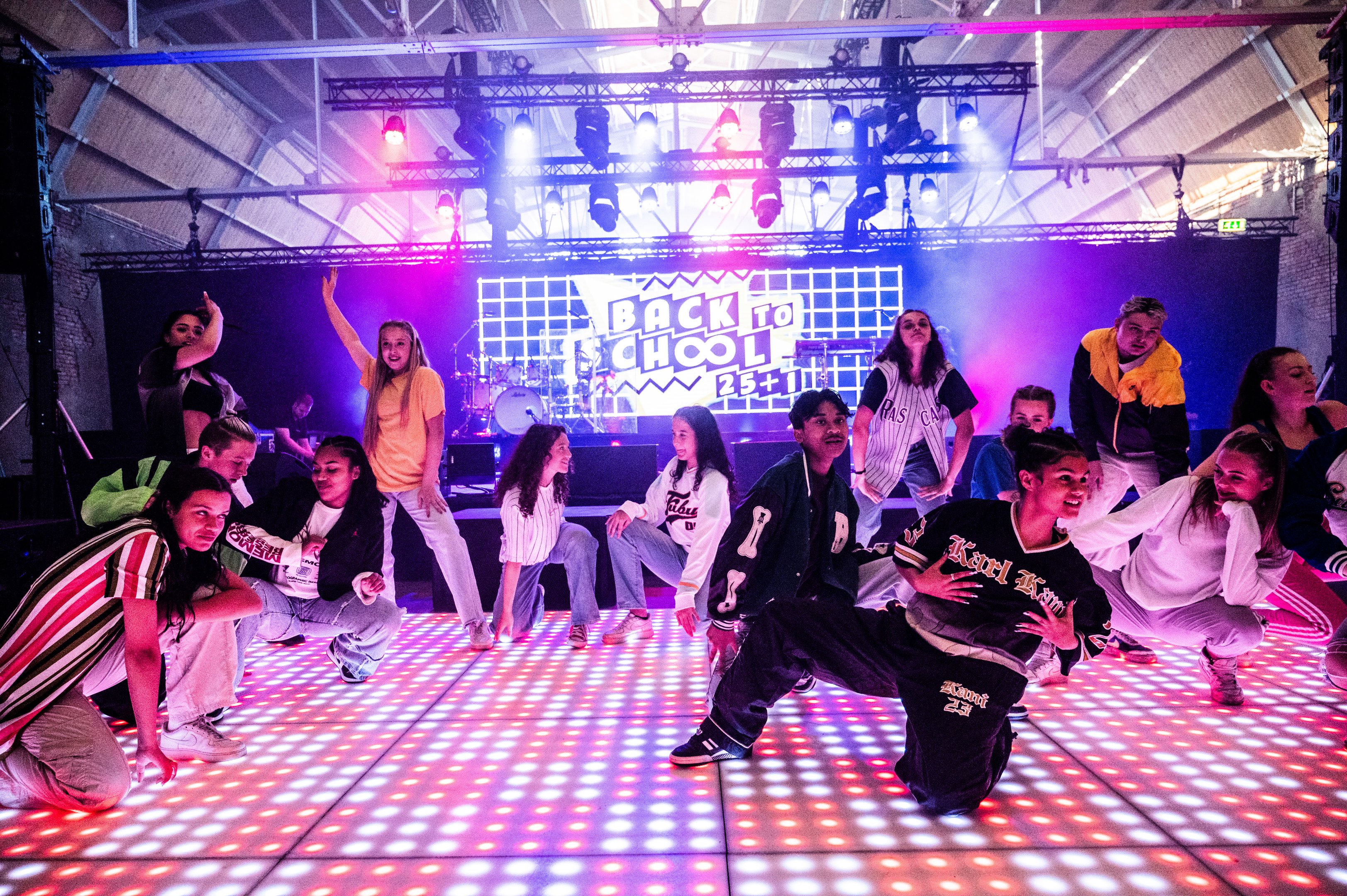 Groep dansende jongeren op verlicht podium tijdens jubileumevenement van onderwijsorganisatie Noorderpoort