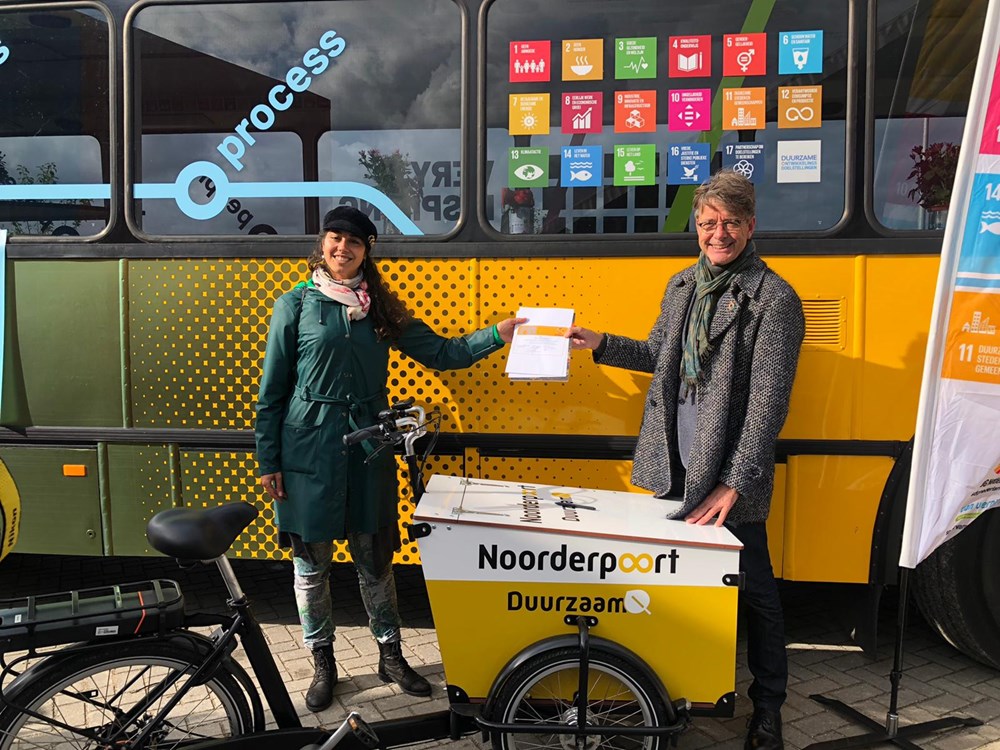 Twee vertegenwoordigers van Noorderpoort overhandigen een document bij duurzame bakfiets voor SDG House