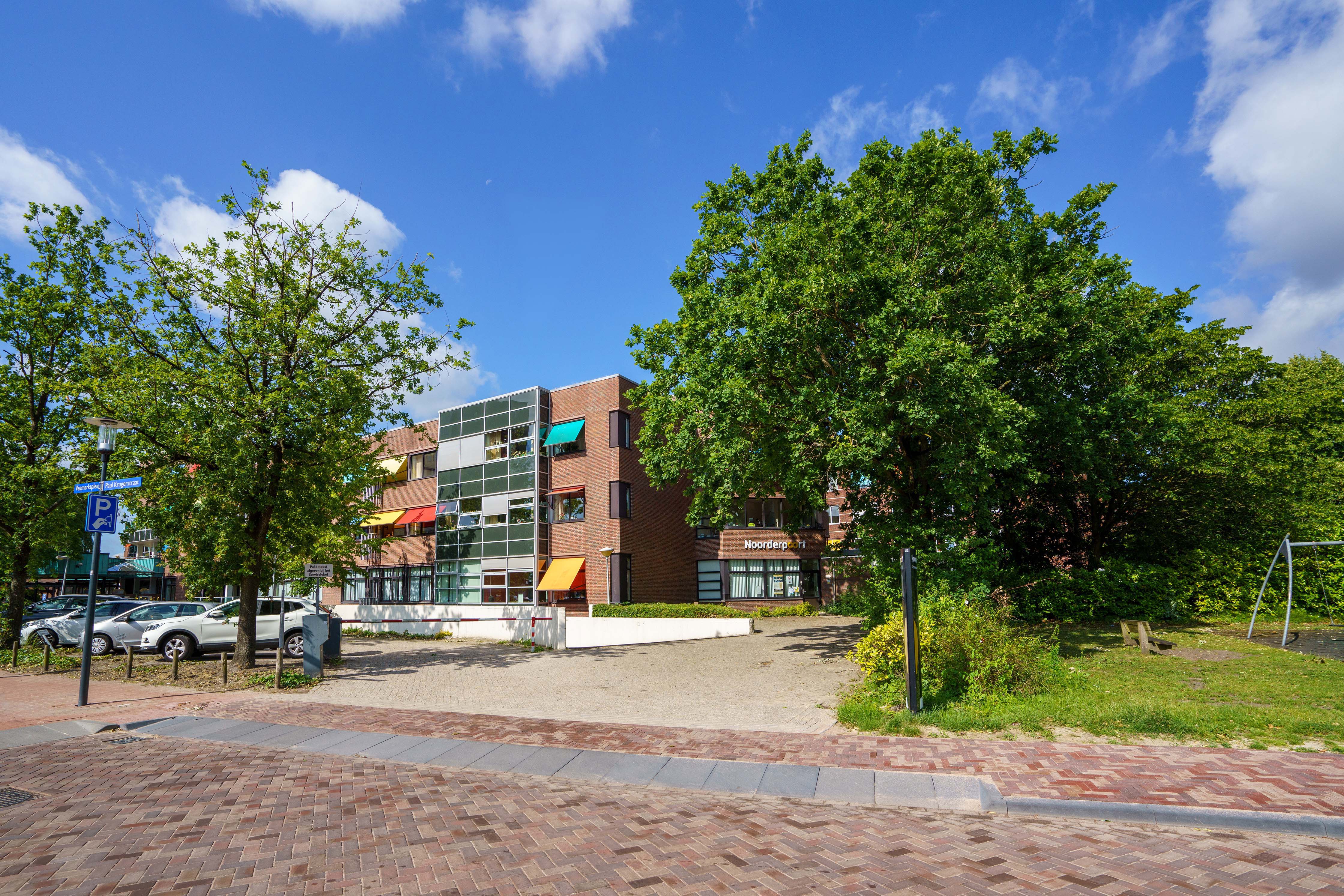 Hoofdgebouw van Noorderpoort aan de Paul Krugerstraat in Assen omgeven door bomen en parkeerplaatsen