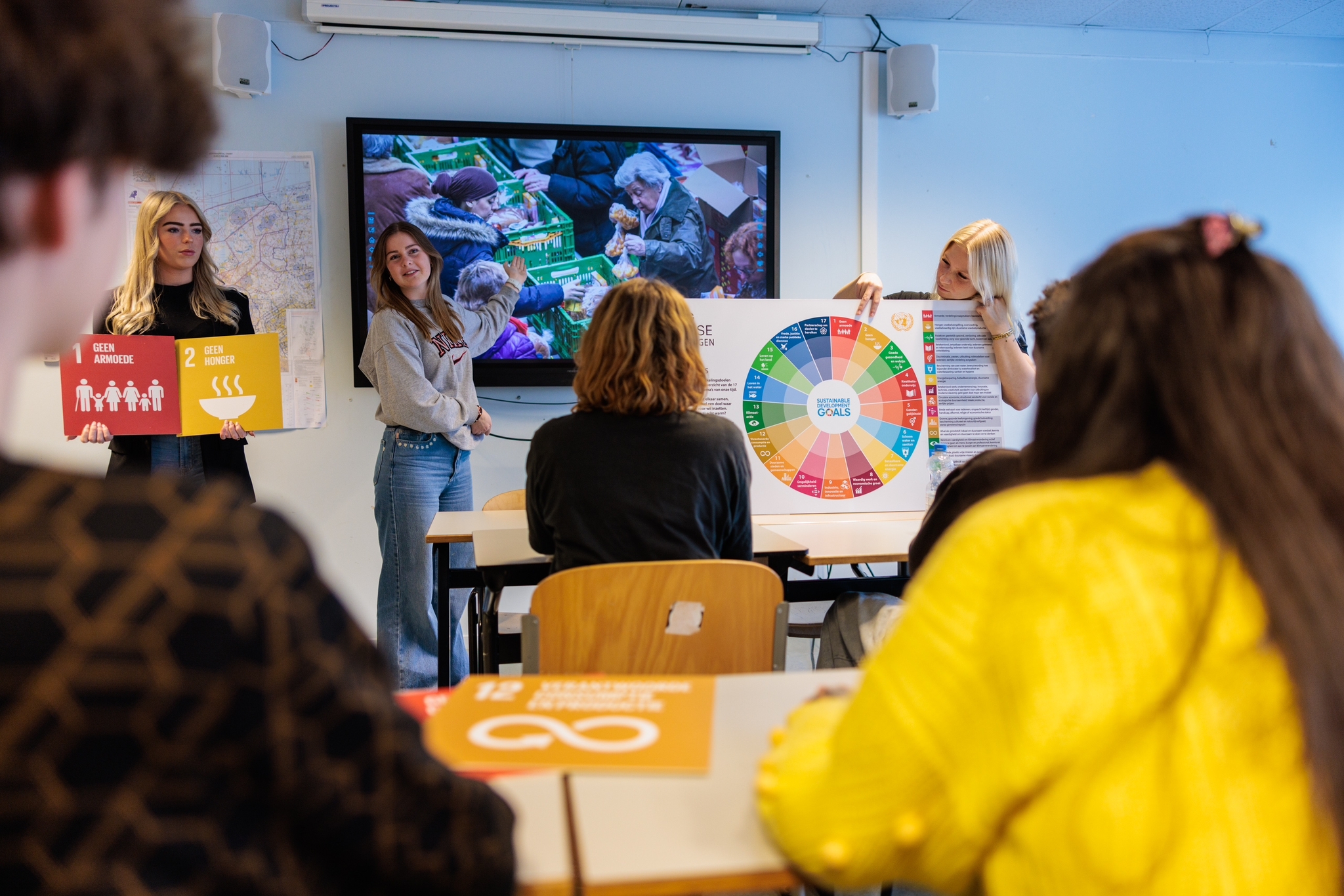 Docenten presenteren een duurzame ontwikkelingsdoelenwijzer aan studenten in een klaslokaal van Noorderpoort.
