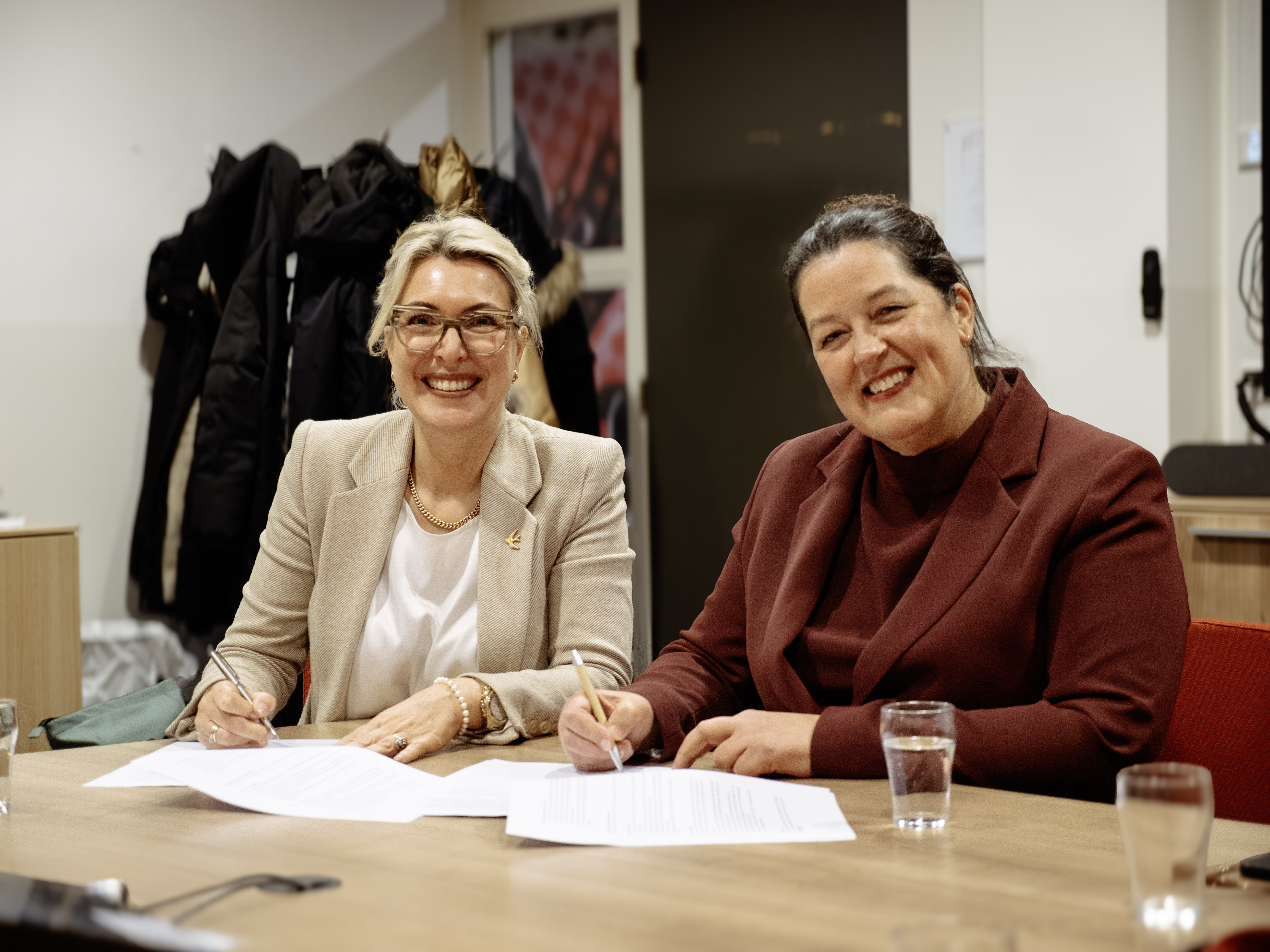 Twee professionals tekenen een samenwerkingsovereenkomst voor zorgonderwijs aan een tafel in een kantoorsetting