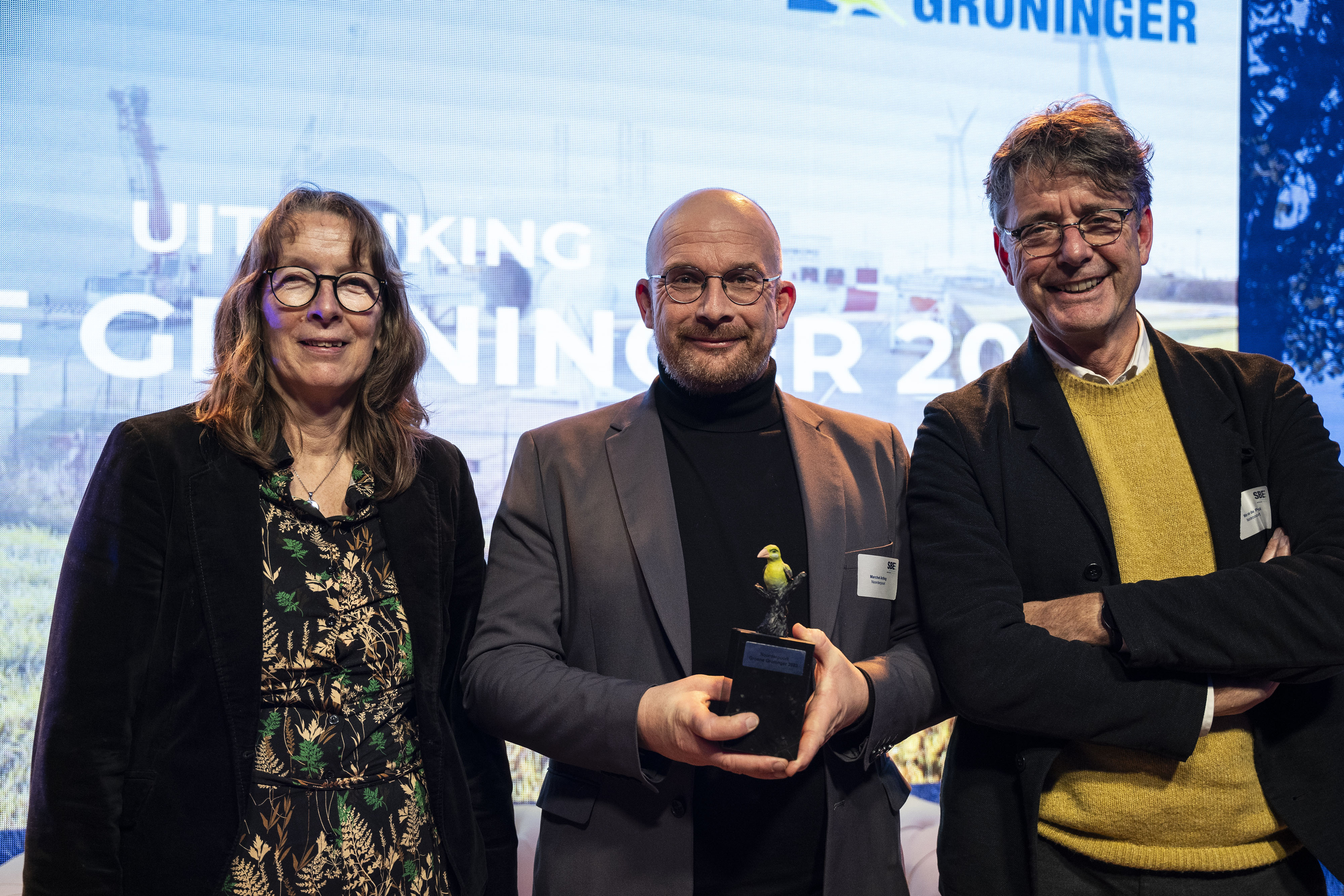 Drie personen op het podium tijdens de uitreiking van de Groene Groninger 2023, waarbij een man een award vasthoudt