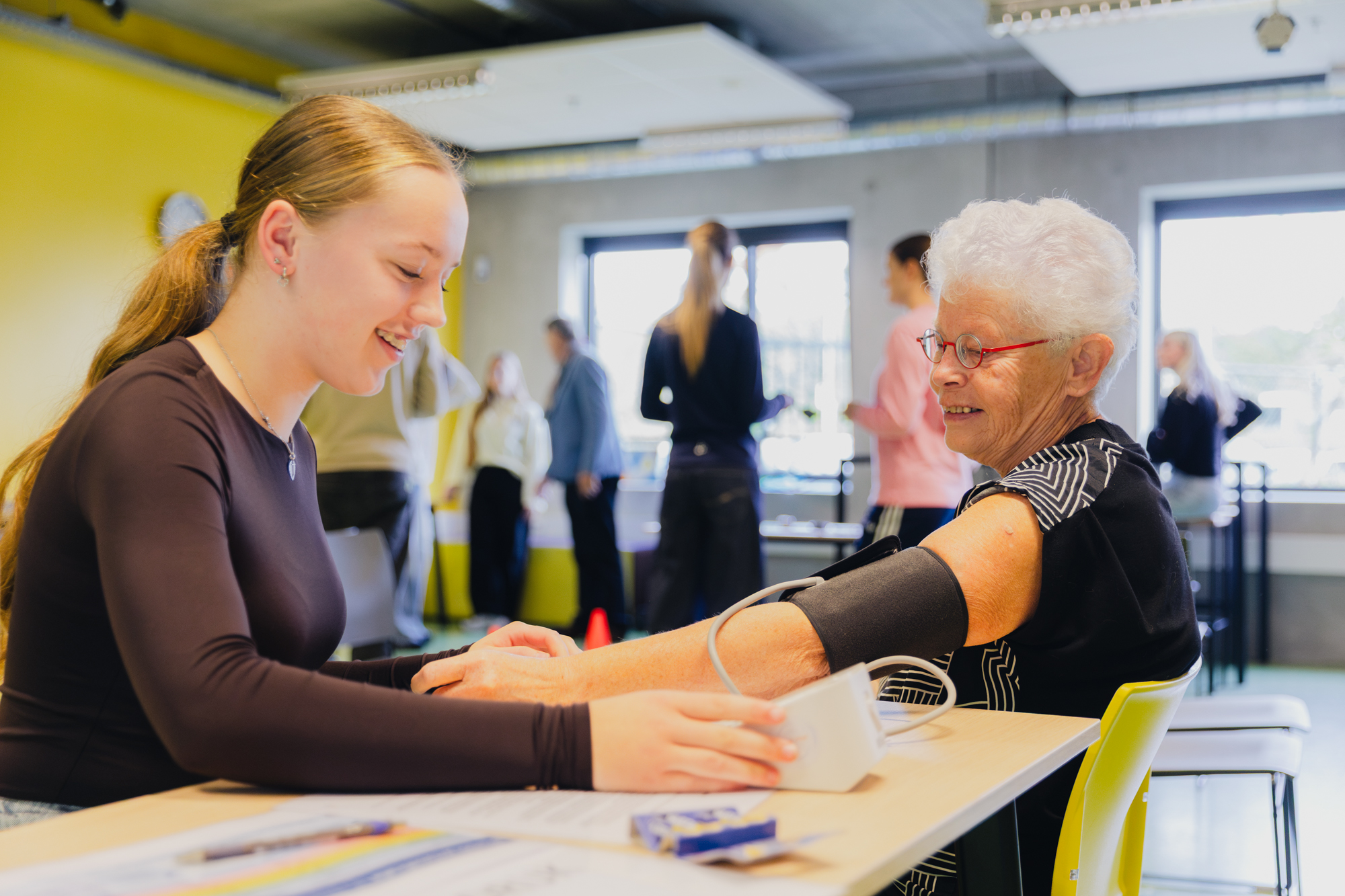 Student begeleidt deelnemer 55-plus bij het meten van bloeddruk tijdens fitheidstest in Winschoten