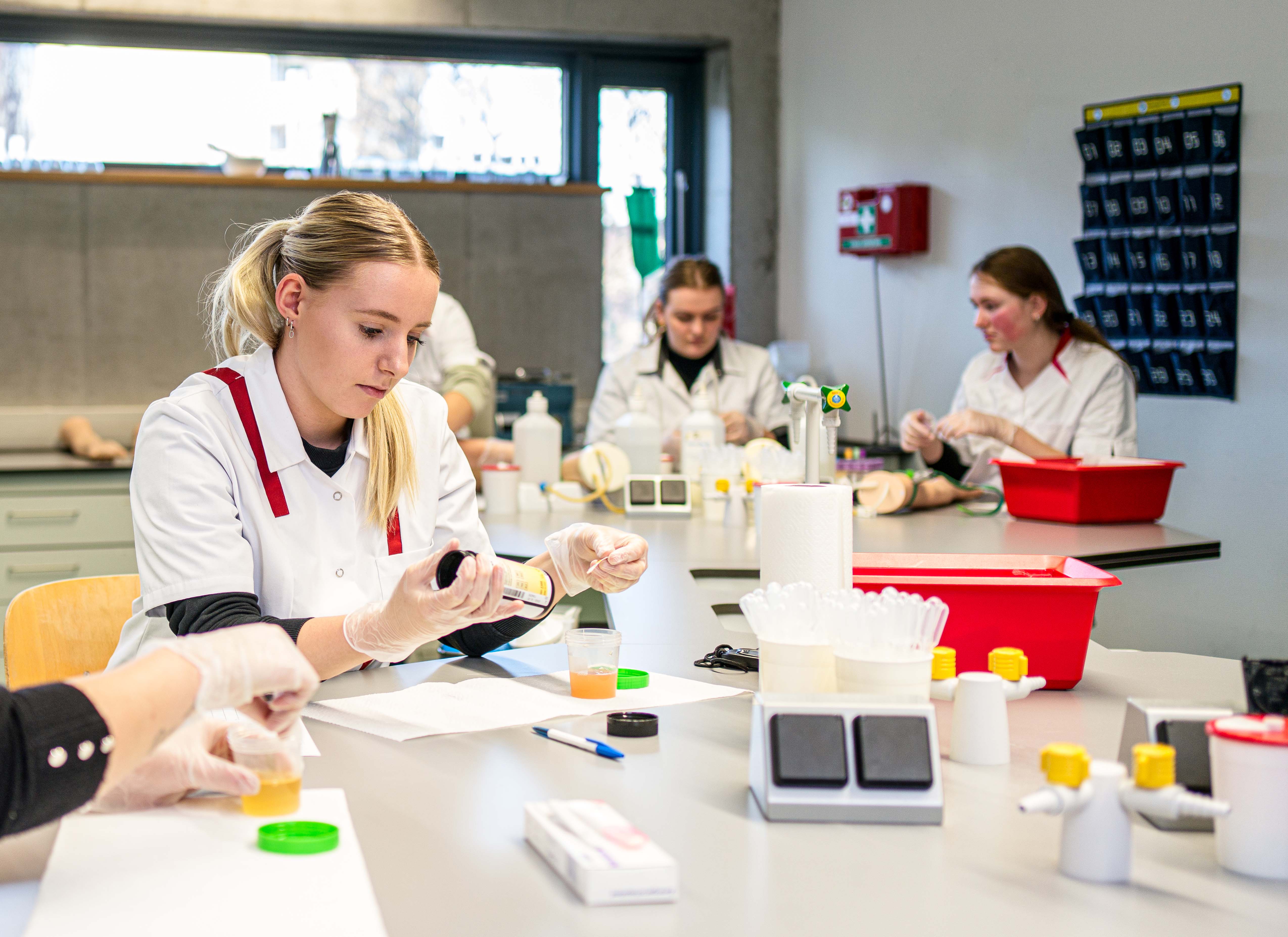 Studenten in witte leren oefenen medische procedures tijdens doktersassistentopleiding in een praktijklokaal