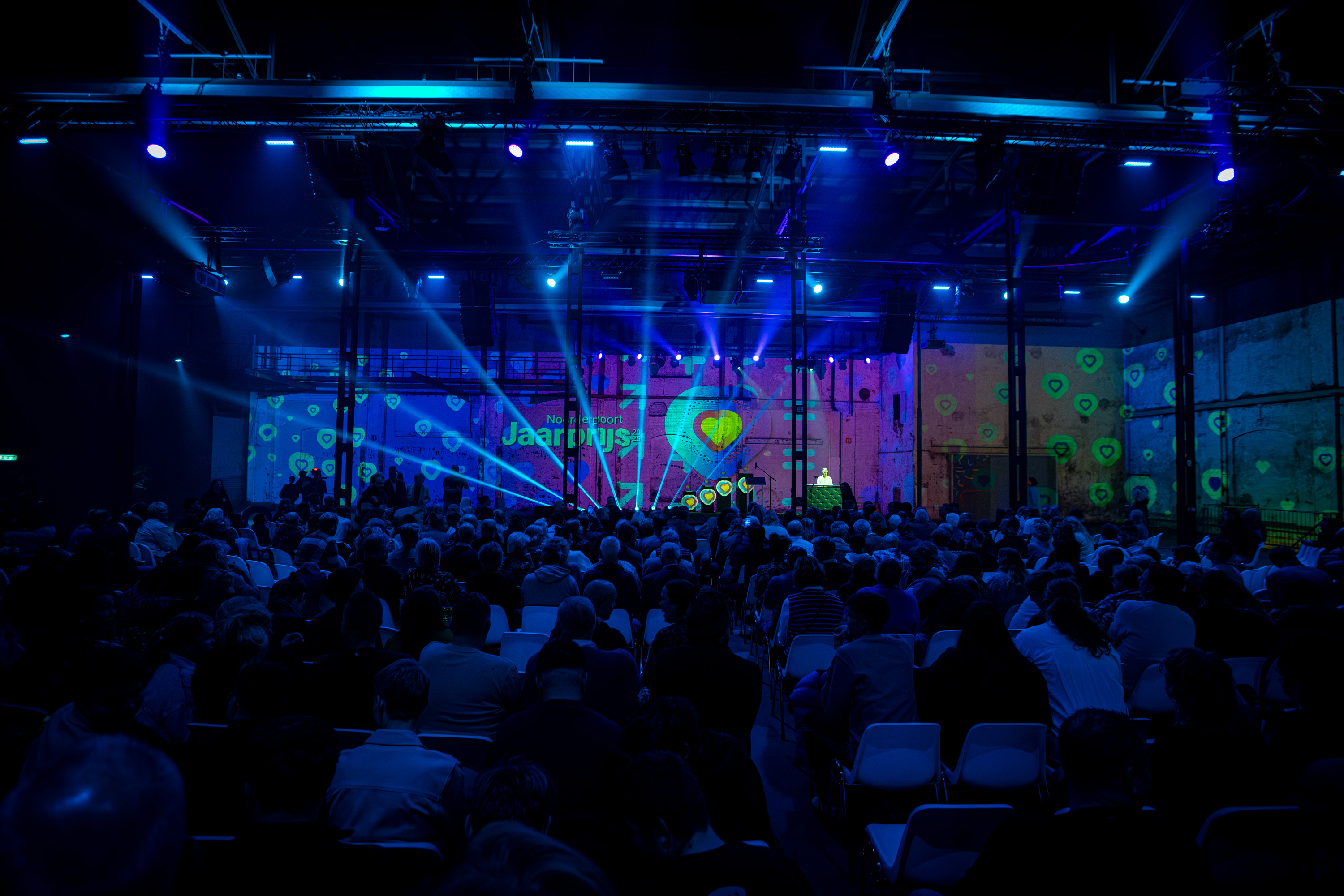 Publiek zit en kijkt naar een podium tijdens de Noorderpoort Jaarprijs 2026 met lichtshow en projecties.