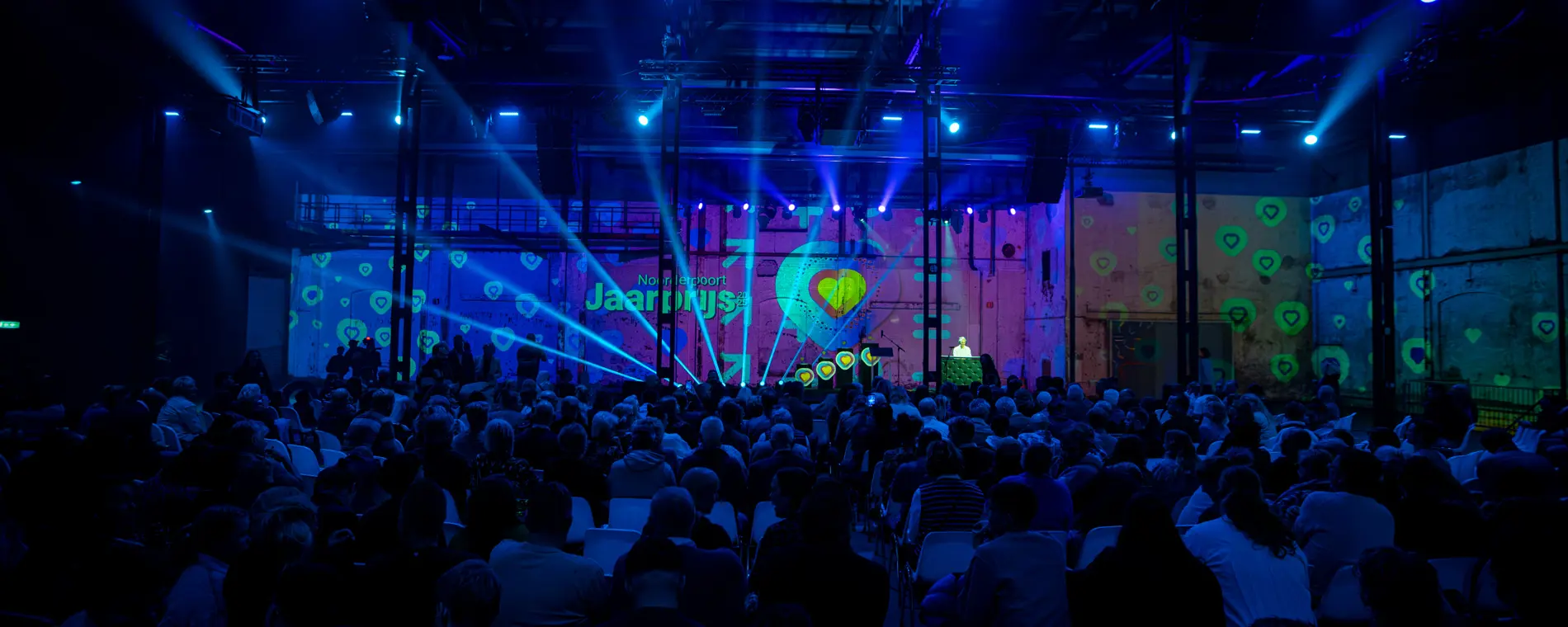 Publiek zit en kijkt naar een podium tijdens de Noorderpoort Jaarprijs 2026 met lichtshow en projecties.