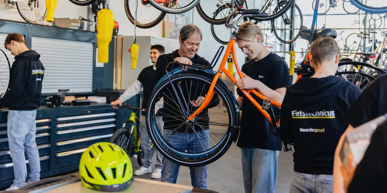Leerlingen en docent repareren samen een fiets tijdens de opleiding fietstechnicus in een werkplaats.
