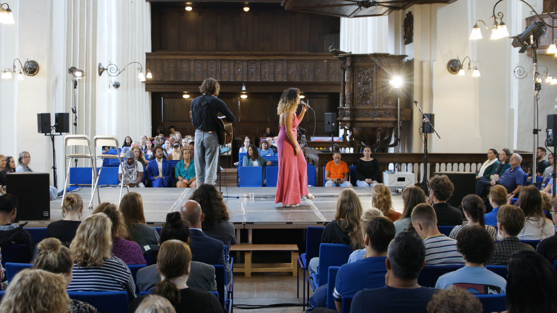 Studenten en medewerkers van Noorderpoort nemen deel aan Keti Koti-event in een kerkzaal met zangoptreden.