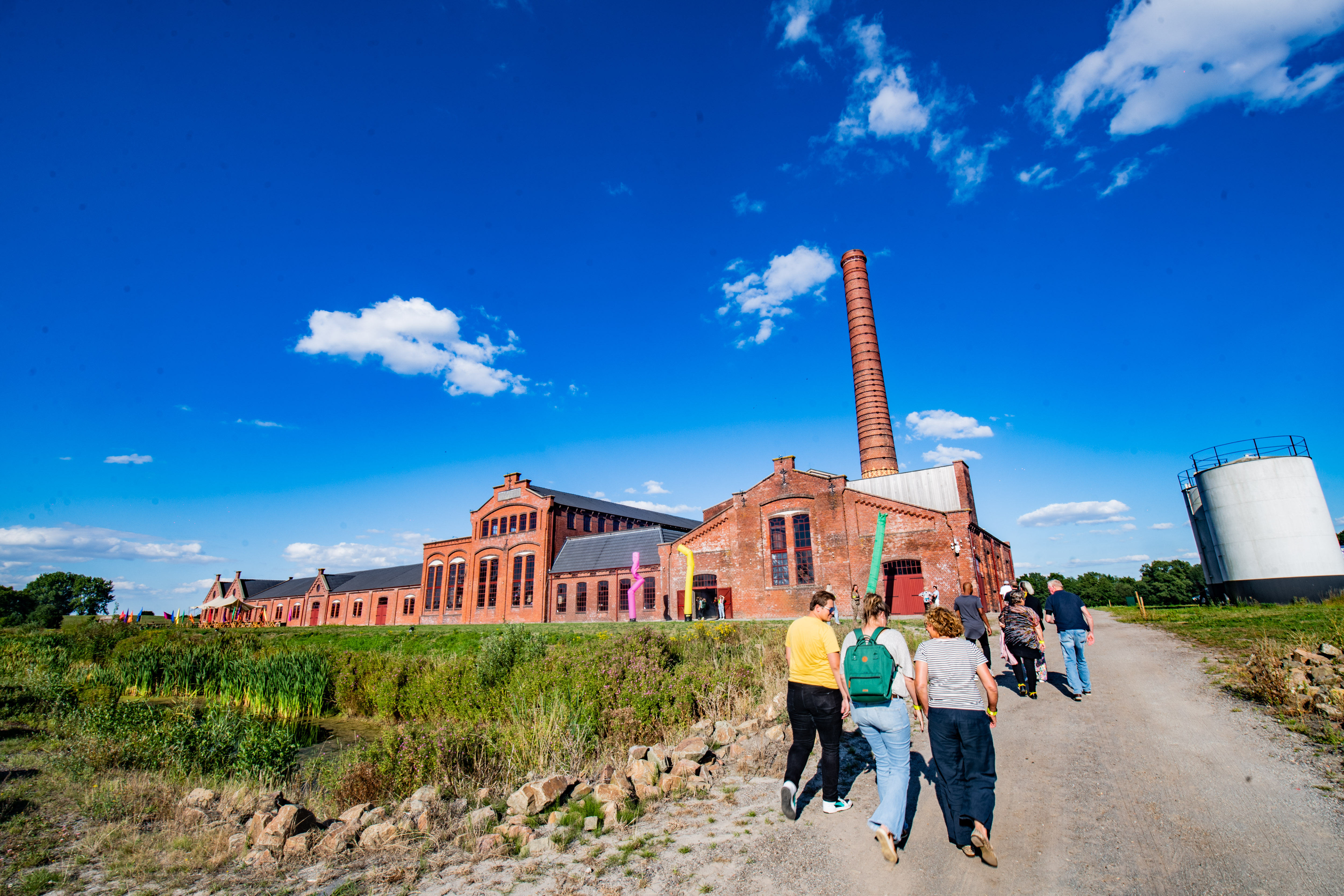 Groep mensen wandelt naar industrieel erfgoedgebouw tijdens jubileumevenement van Noorderpoort.