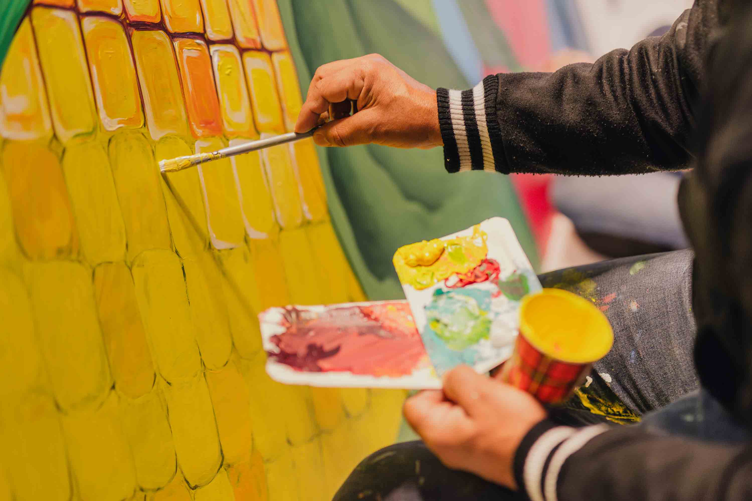 Kunststudent brengt geeltinten aan op muurschildering als onderdeel van kunst en wetenschap project