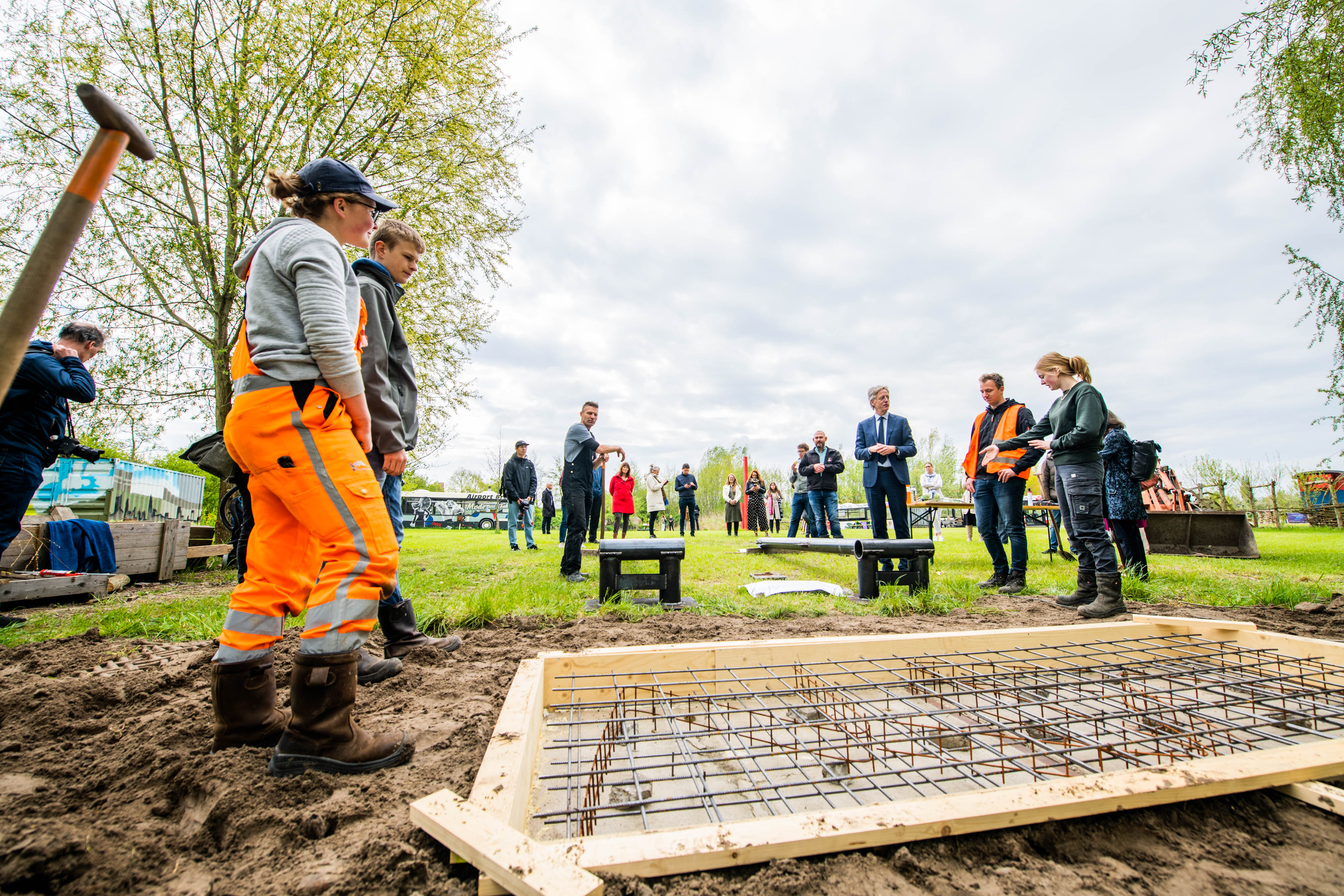 Groep professionals en studenten staan buiten rond een bouwplaats en bespreken duurzame samenwerkingsprojecten in het onderwijs