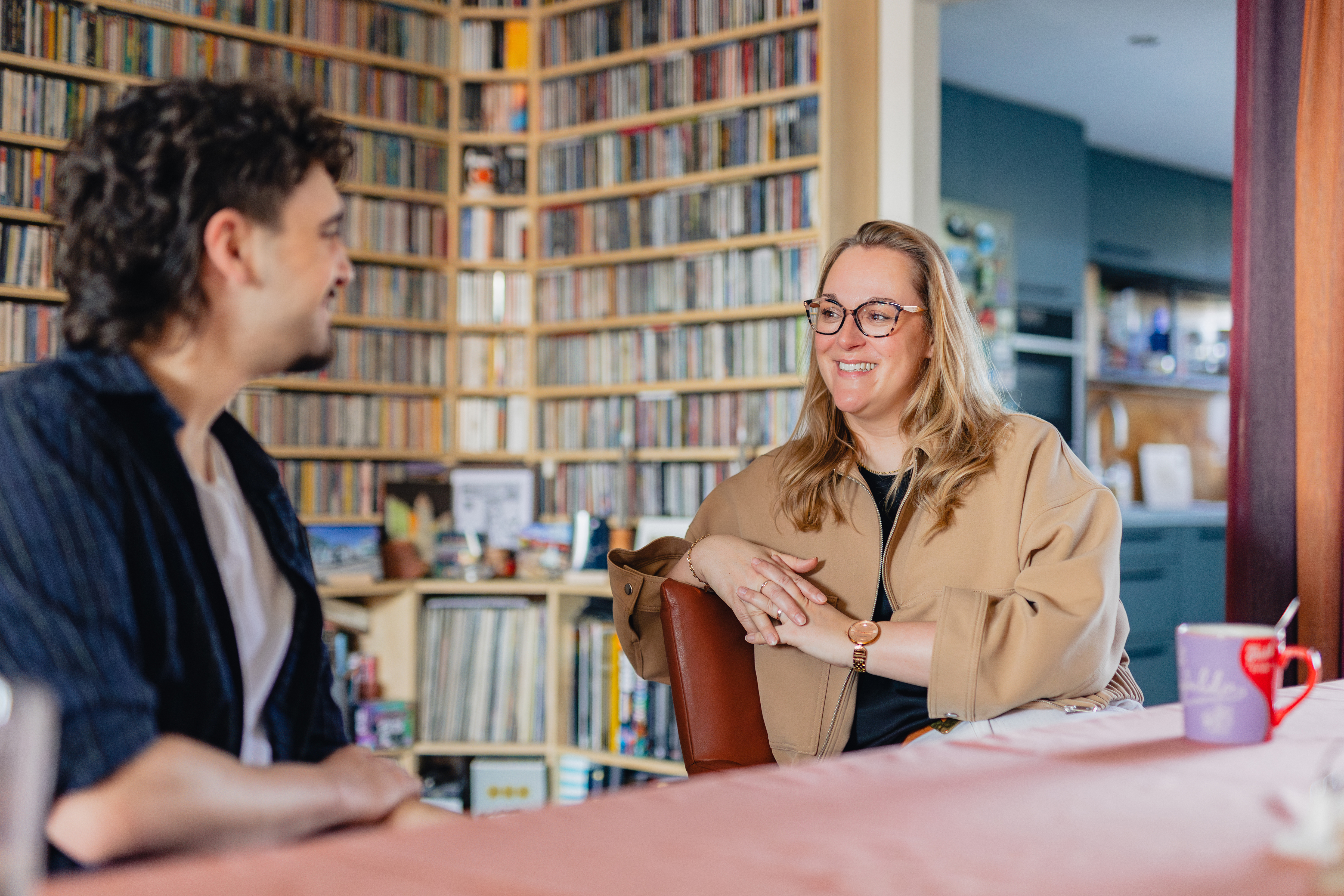 Twee personen voeren een inspirerend gesprek aan tafel in een omgeving met boekenkasten, passend bij studiekeuzeadvies.