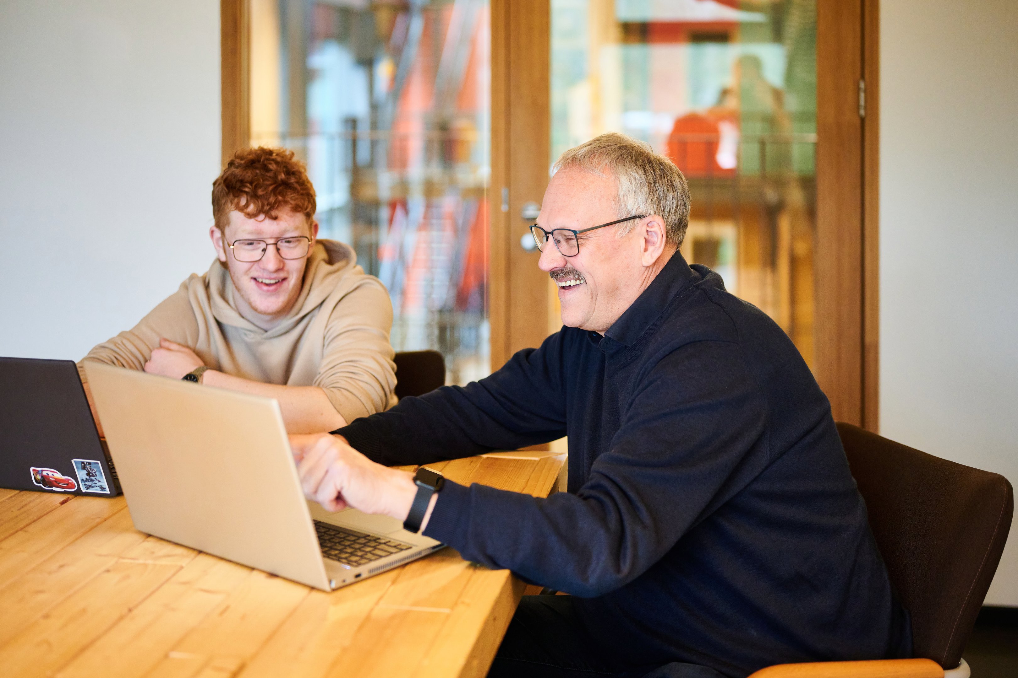 Docent begeleidt een student tijdens een interactieve leersessie met laptops aan een houten tafel