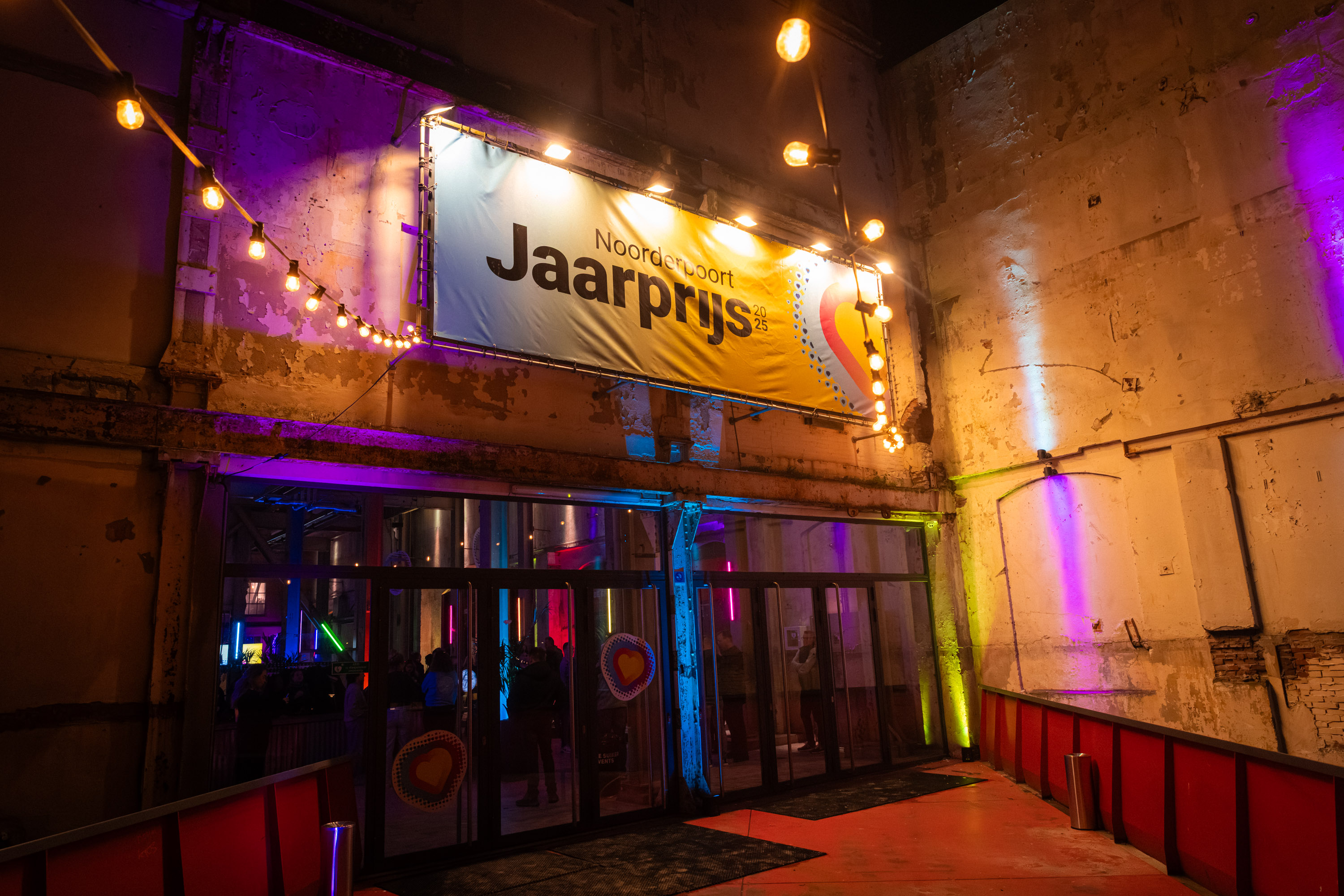 Ingang van een evenementlocatie met banner 'Noorderpoort Jaarprijs' verlicht door sfeerverlichting