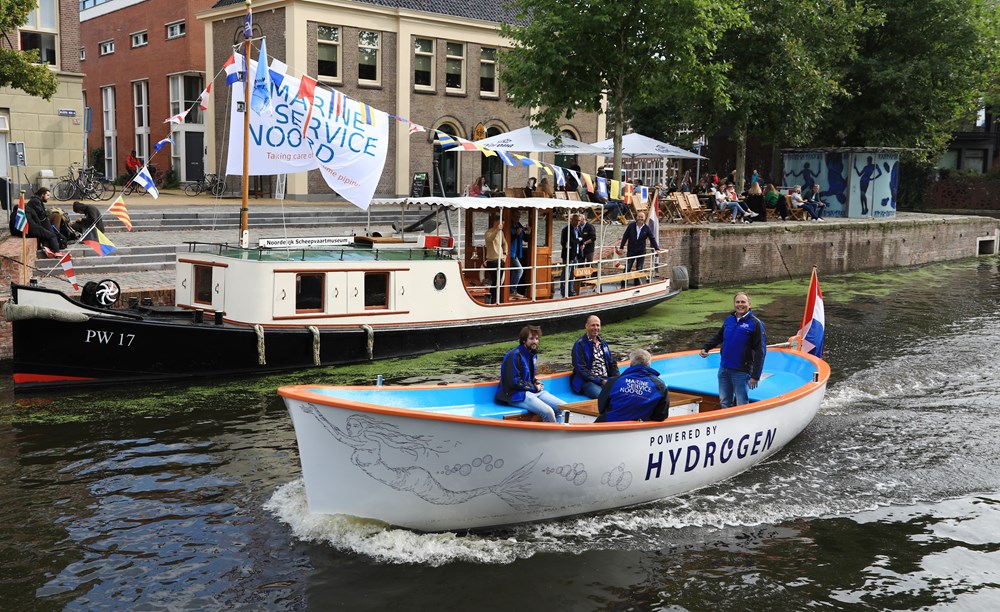 Een sloep op waterstof met bemanning vaart door een grachtengebied tijdens een duurzaamheidsproject.