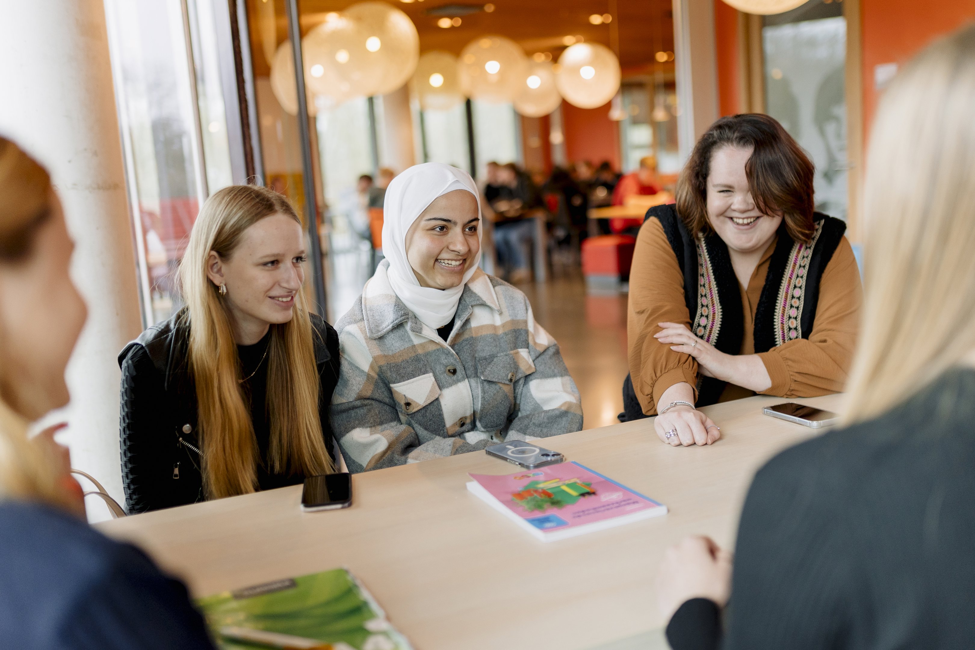 Studenten praten ontspannen aan een tafel tijdens een educatieve bijeenkomst bij Noorderpoort.
