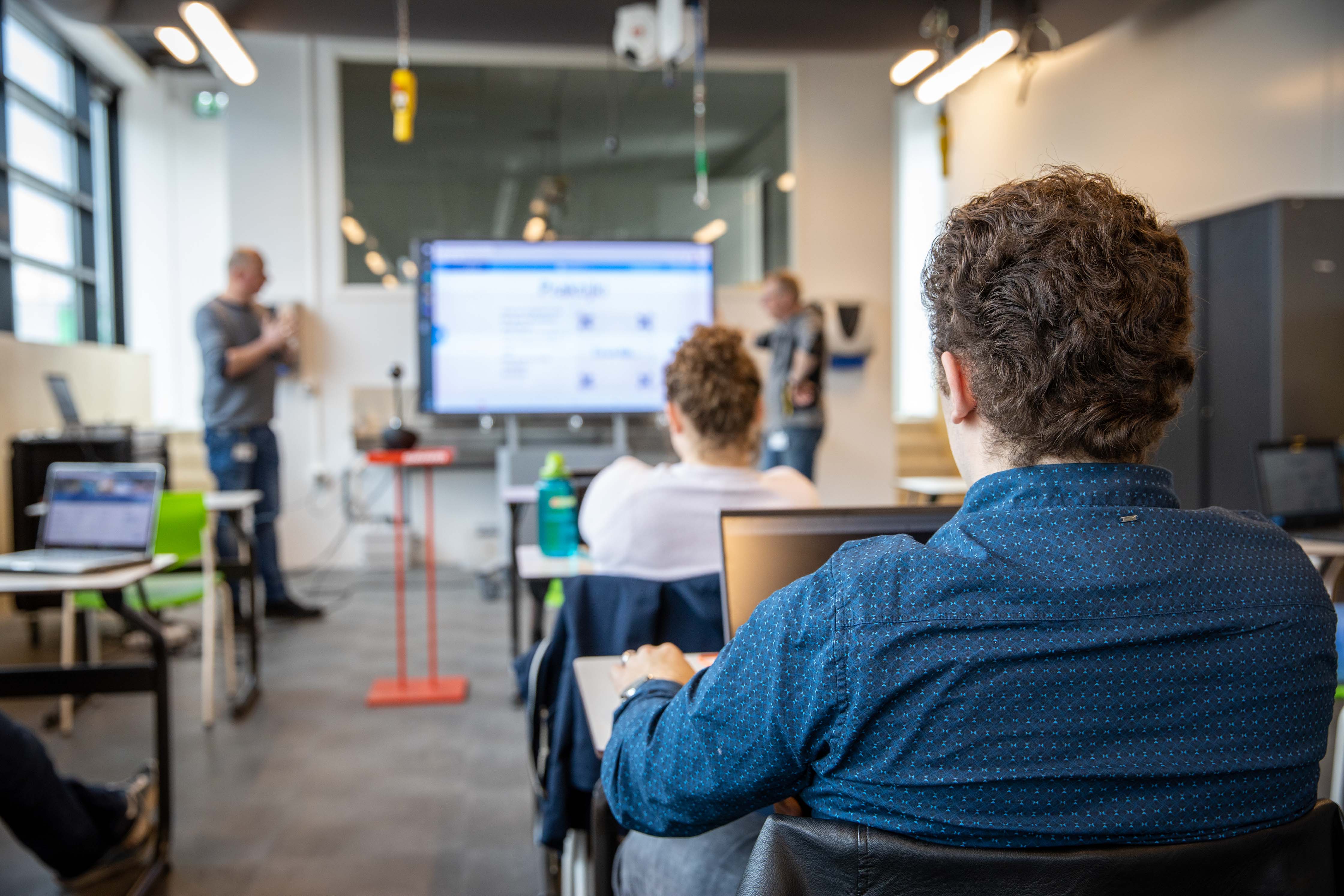 Studenten zitten in een klaslokaal en luisteren naar een docent die een presentatie geeft over digitale vaardigheden.