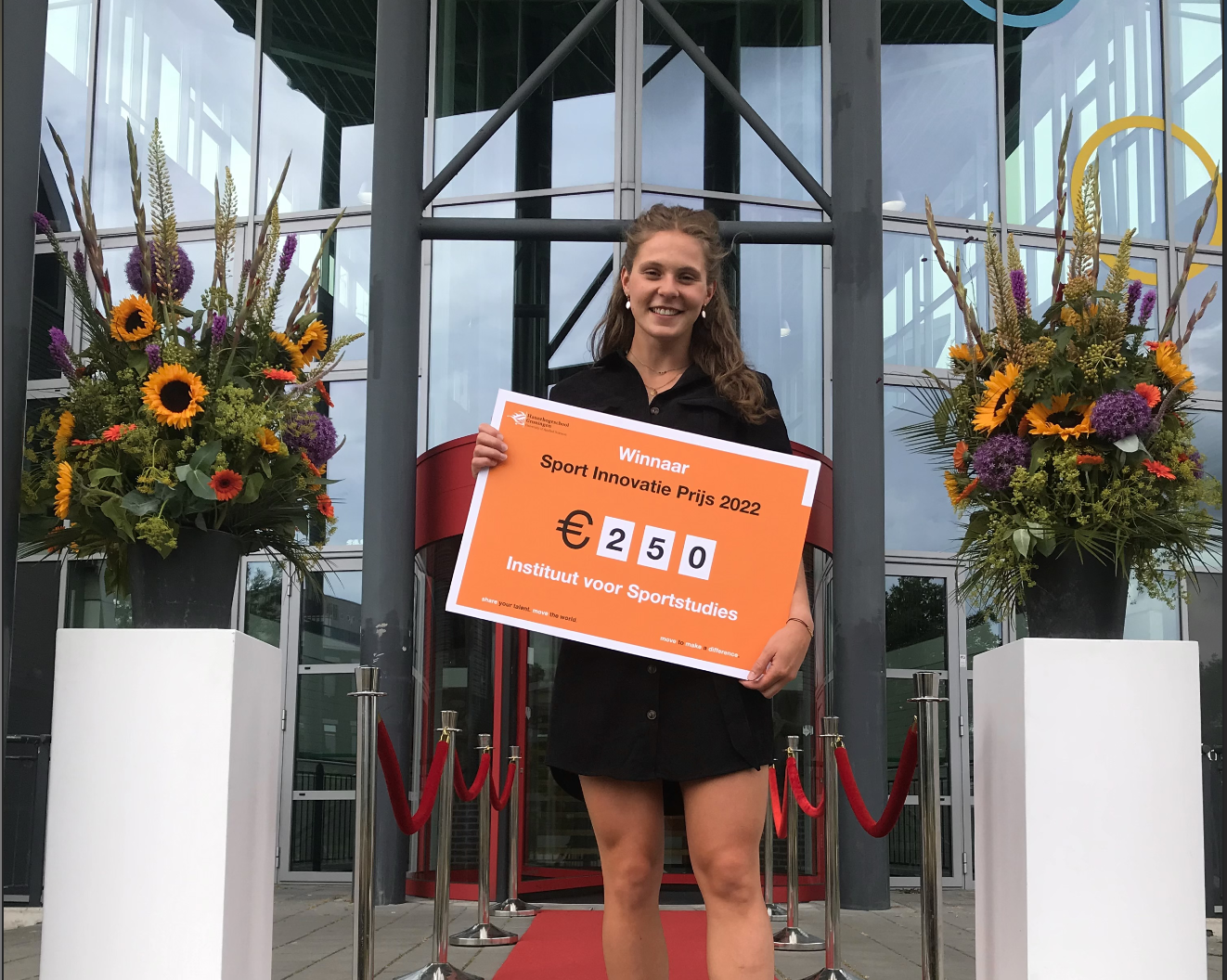Student ontvangt Sport Innovatie Prijs 2022 van Instituut voor Sportstudies bij de entree van een onderwijsgebouw