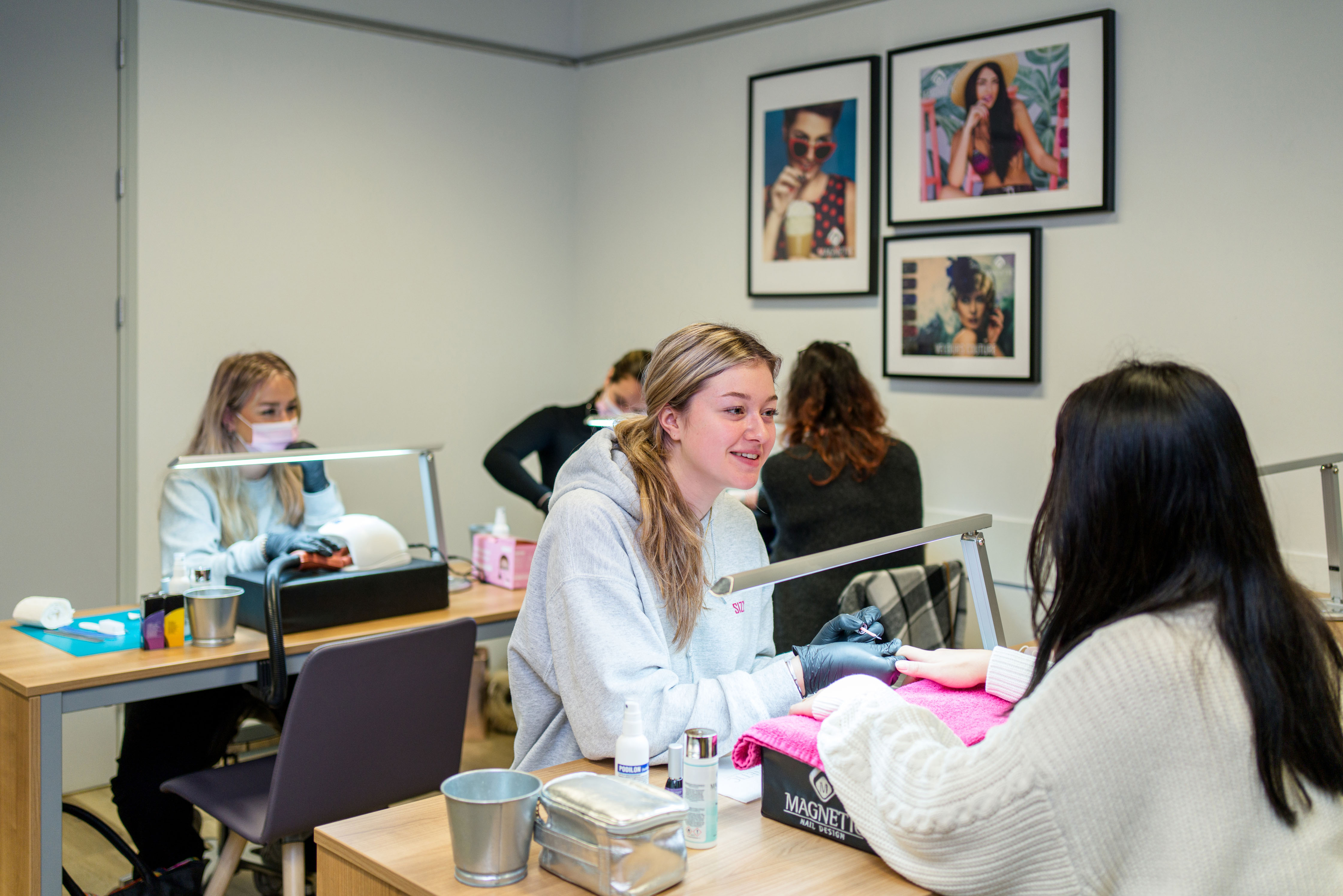 Student ontvangt verzorging aan tafel tijdens praktijkles uiterlijke verzorging in onderwijsruimte