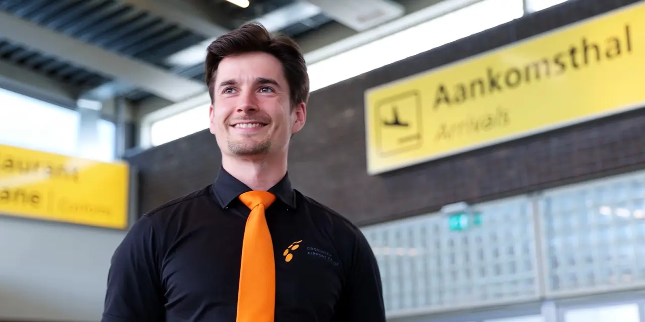 Student staat in aankomsthal en straalt vertrouwen uit met Noorderpoort-logo op zijn overhemd