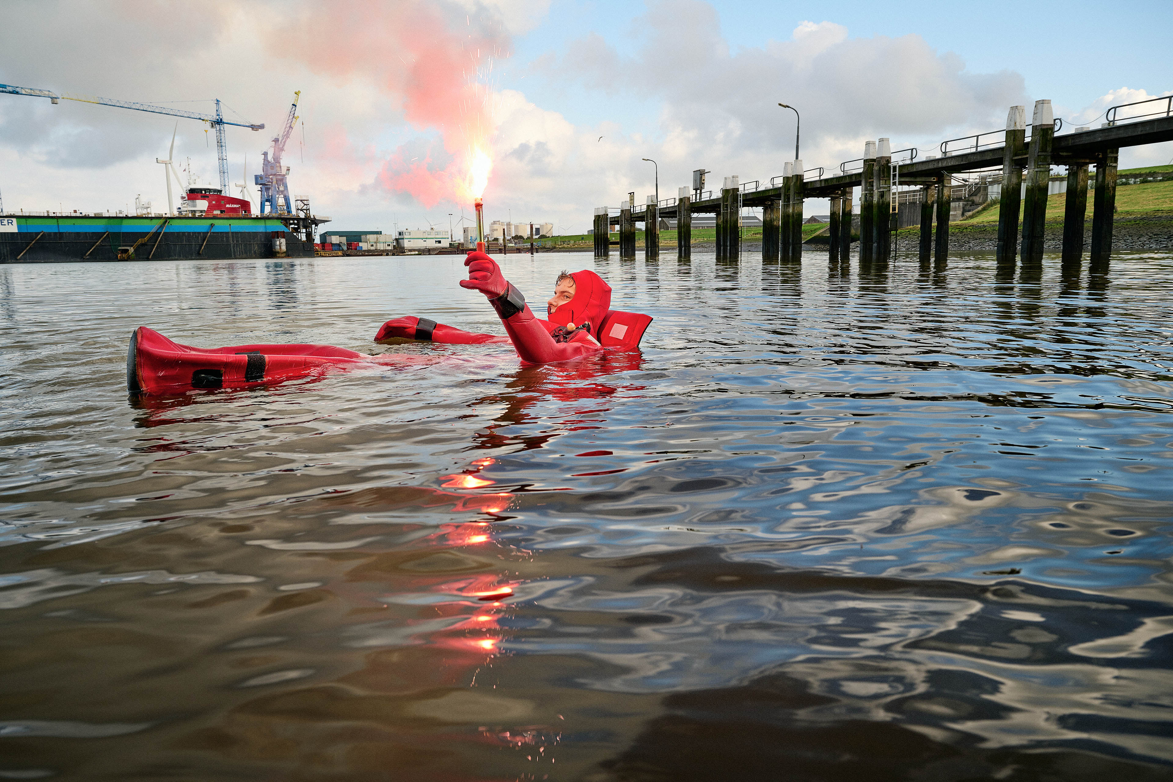 Persoon in drijfpak oefent met noodsignaal op open water, training gericht op veiligheid en zelfredzaamheid.