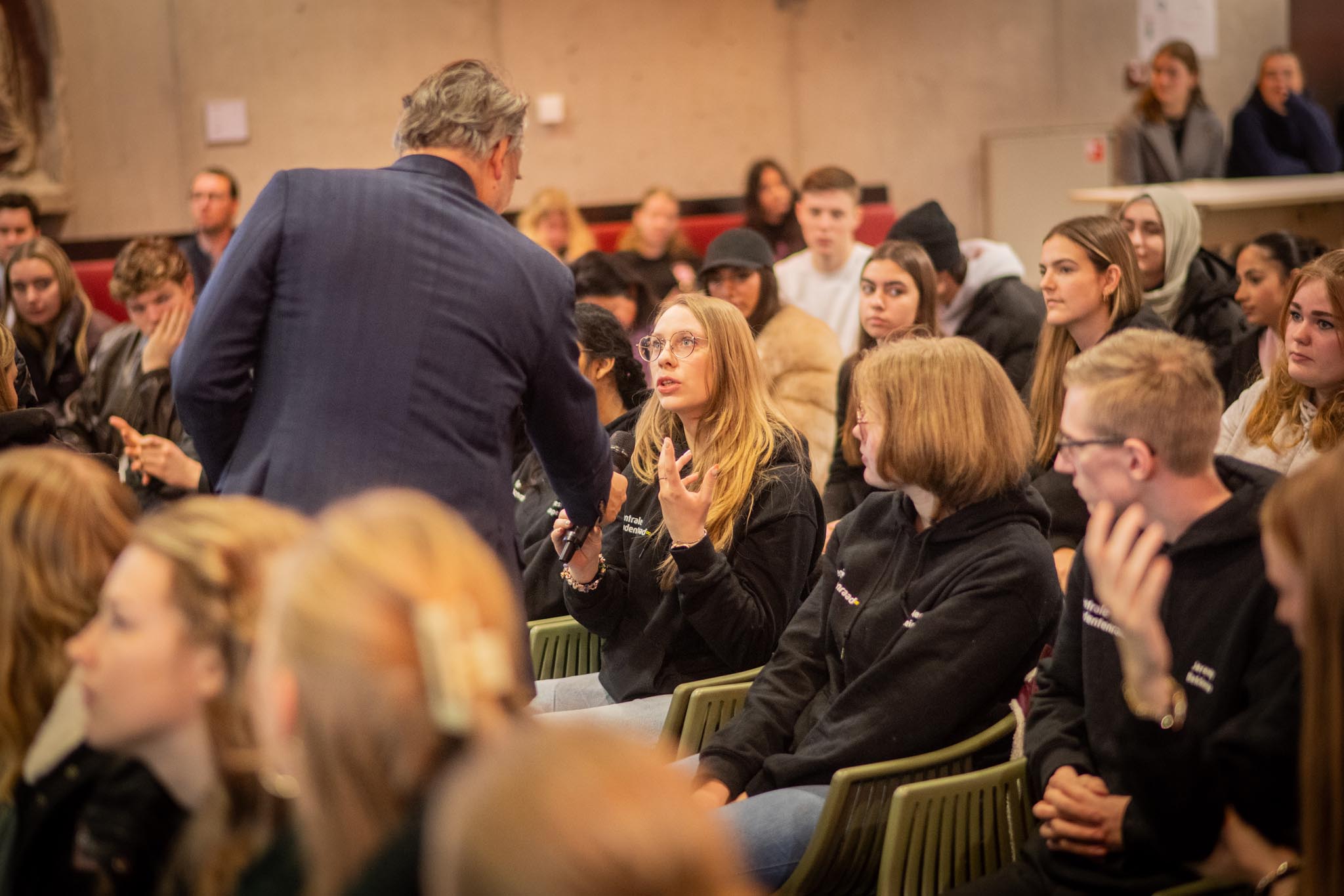 Gesprek tussen een onderwijsbestuurder en aandachtige studenten tijdens bijeenkomst over onderwijs en studentenvragen