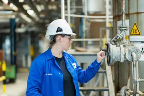 Leerling in technisch veiligheidskleding bedient een industriële klep tijdens een praktijkles procesoperator.
