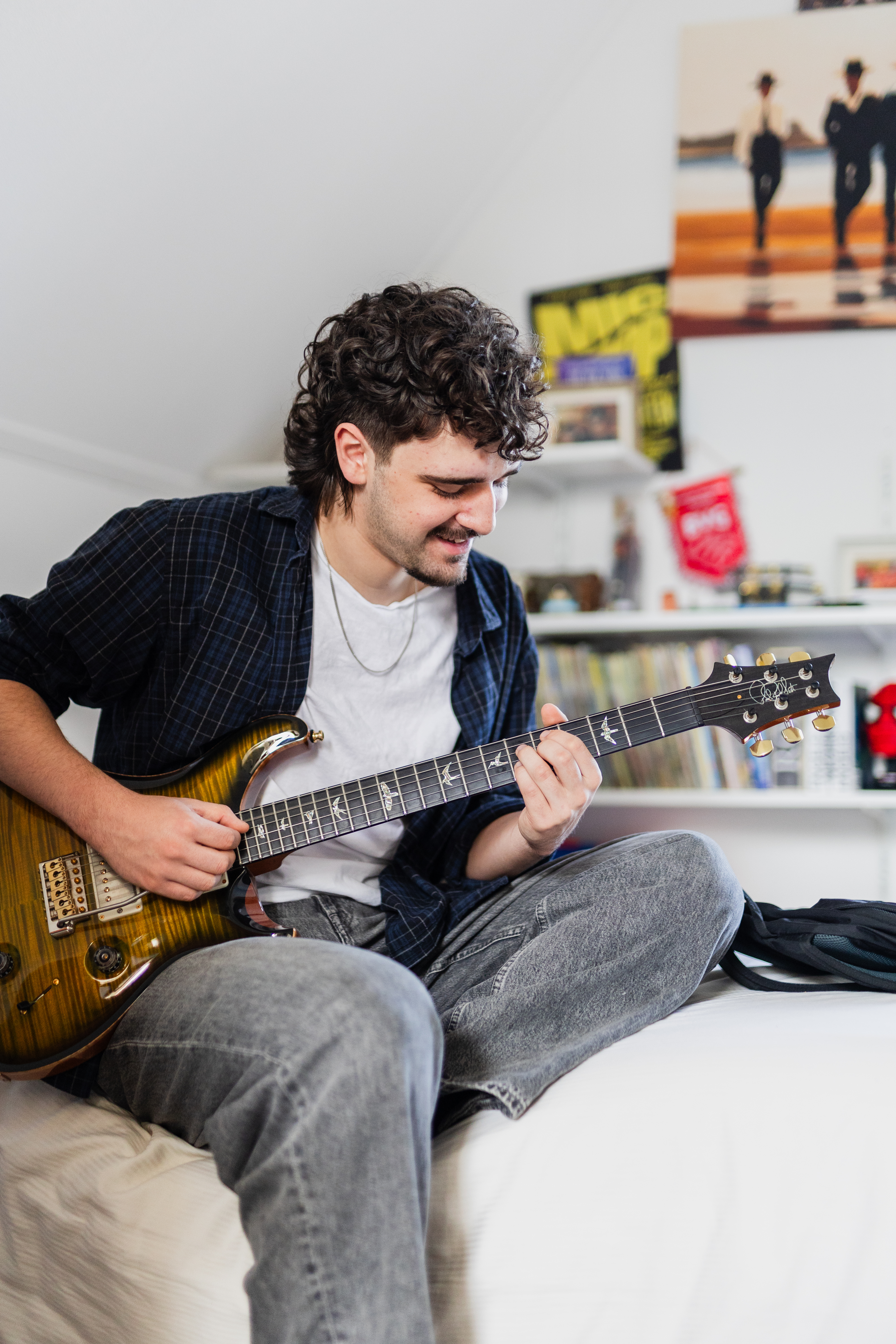 Student oefent gitaar spelen in een slaapkamer met muziekposters op de achtergrond
