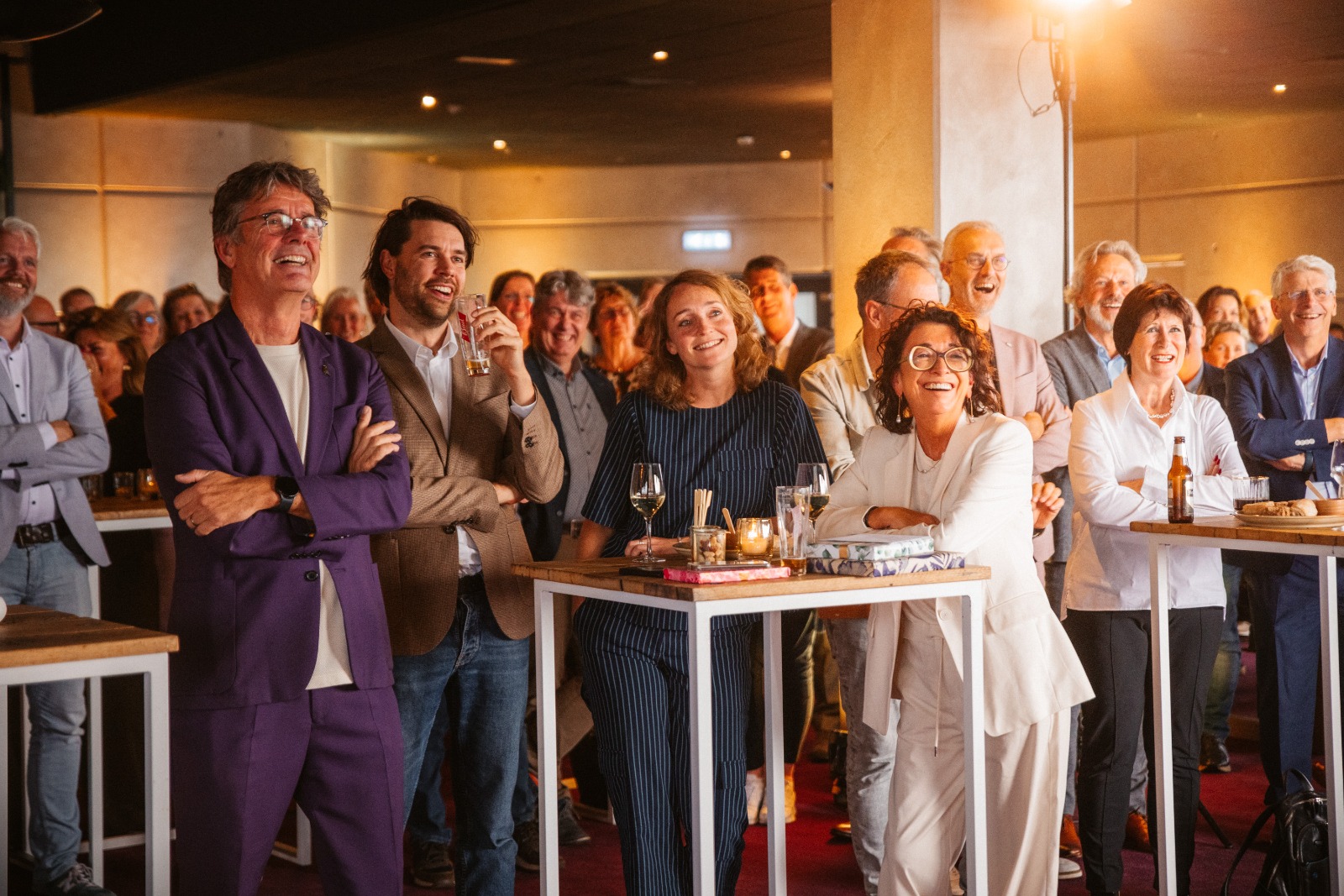 Groep bezoekers luistert aandachtig tijdens evenement, met focus op gezellig samenzijn en netwerken.