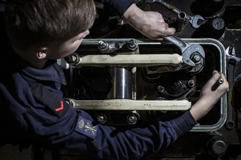 Technische student werkt aan marinetechniek en onderhoudt complexe machineonderdelen aan boord.