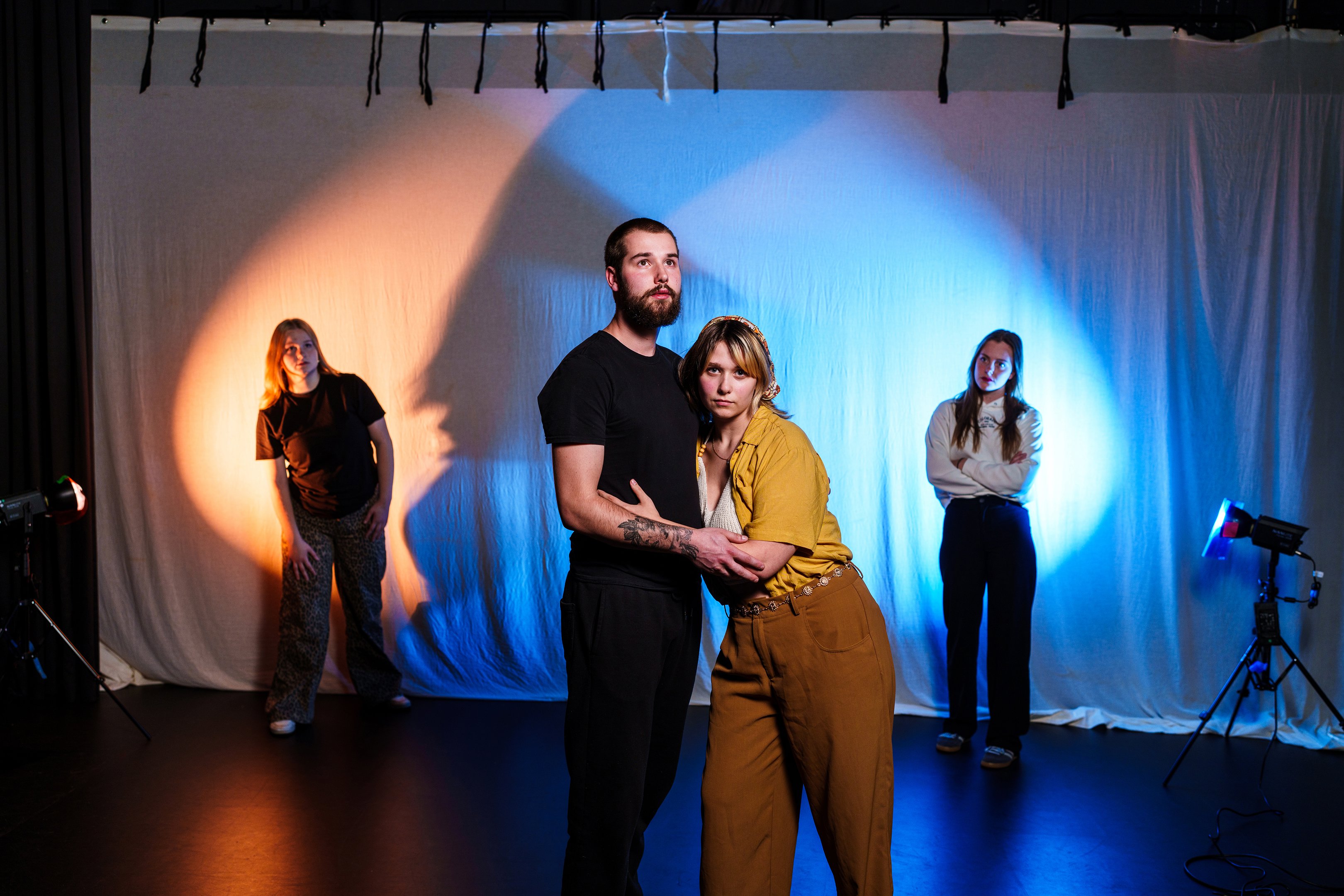 Acteurs oefenen een scène met expressieve lichaamstaal in een theaterstudio met gekleurde verlichting.