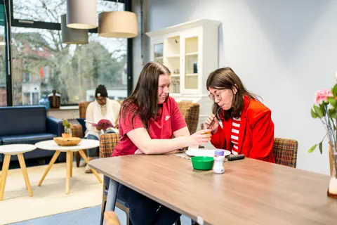 Begeleider maatschappelijke zorg ondersteunt cliënt tijdens sociale activiteit in een woonruimte