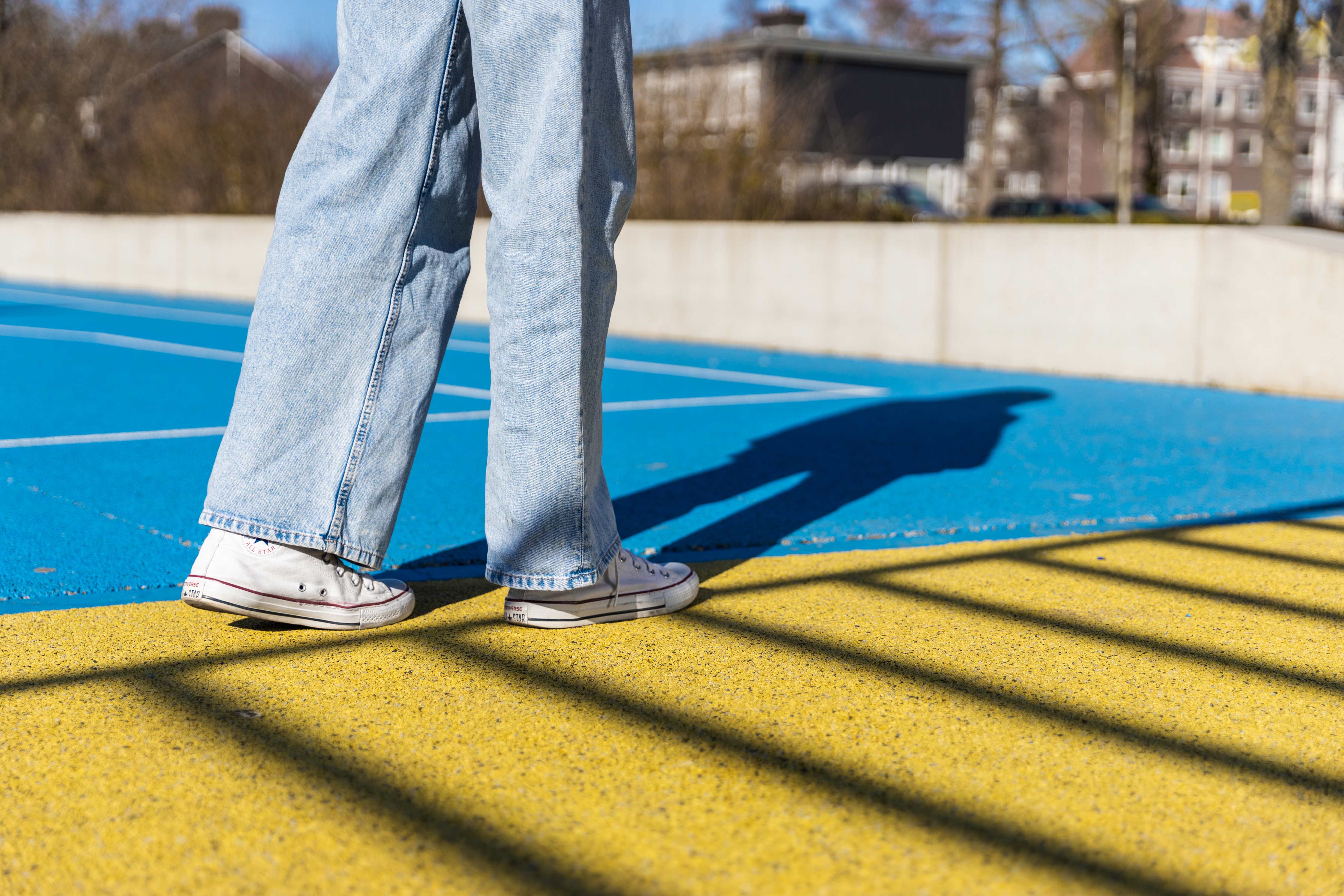 Persoon loopt over een kleurrijk sportveld met blauwe en gele ondergrond bij helder weer