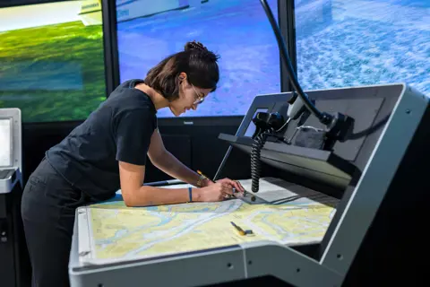Student controleert kaart in nautische simulator voor kleine schepen bij Maritiem officier opleiding