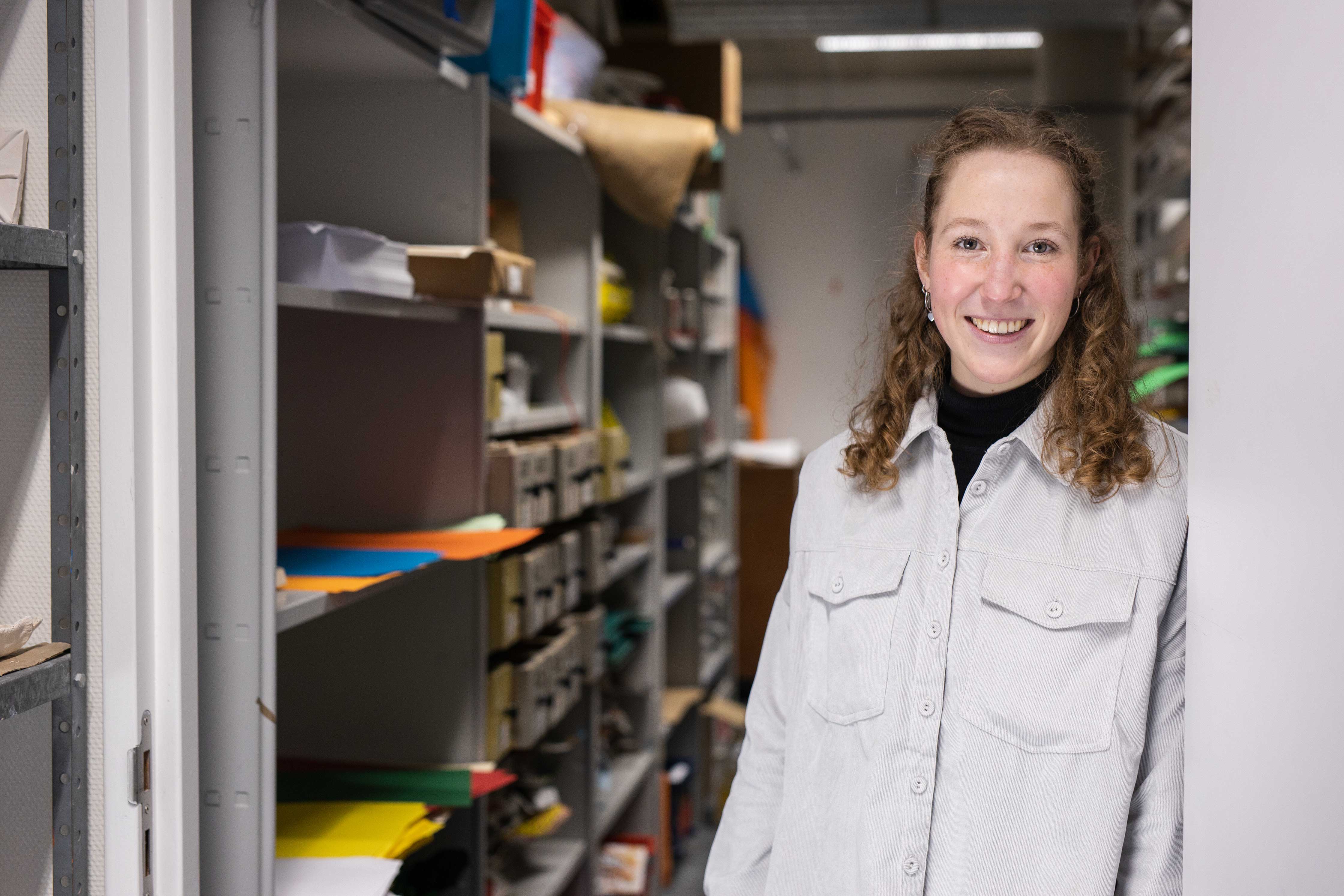 Student die in een opslagruimte met studie- en projectmaterialen staat, klaar om aan een opdracht te werken