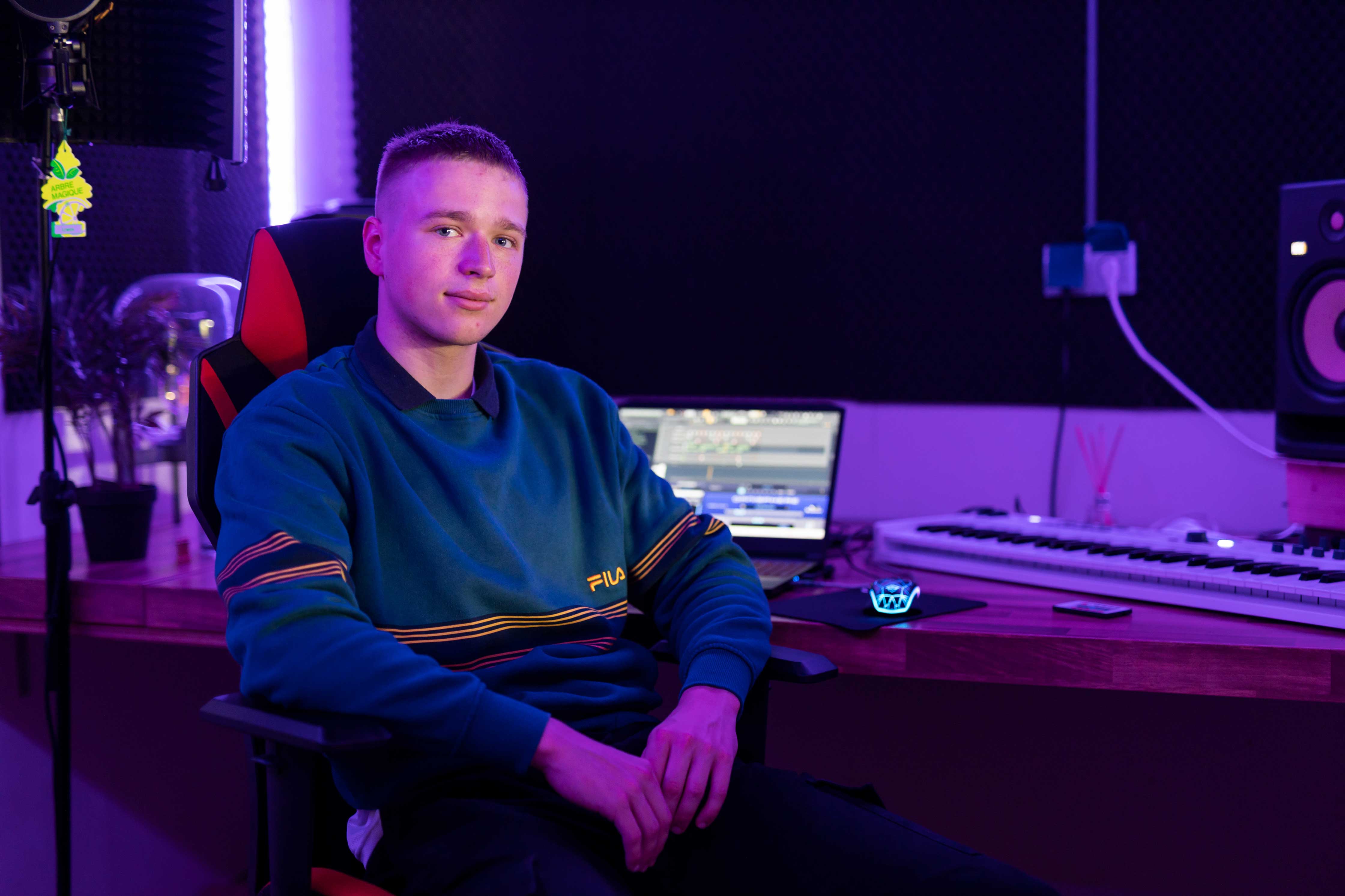 Student zit ontspannen in studioruimte met muziekproductieapparatuur en laptop op bureau
