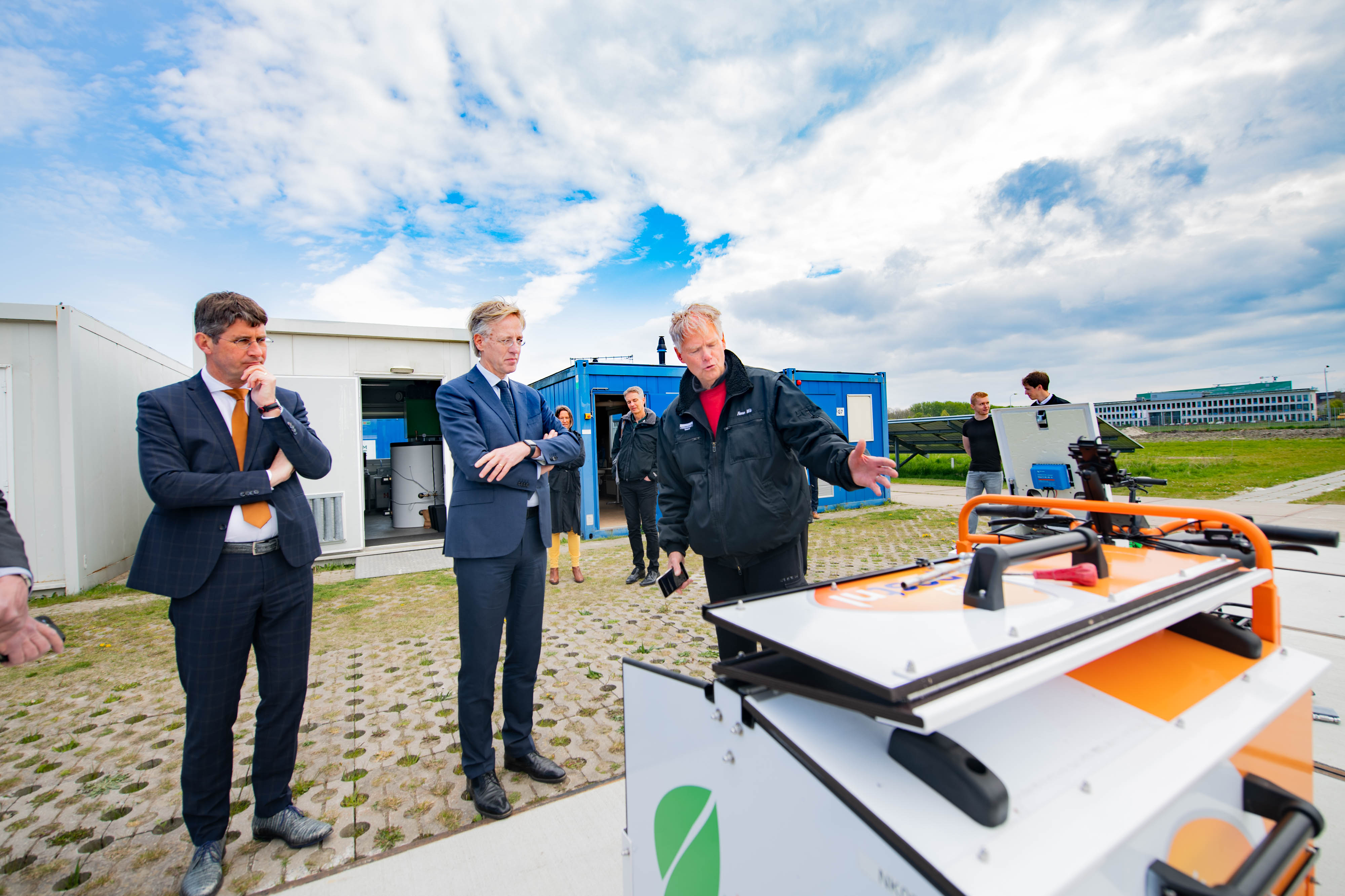 Minister in gesprek met onderwijsprofessionals tijdens demonstratie van duurzame techniek op schoolterrein