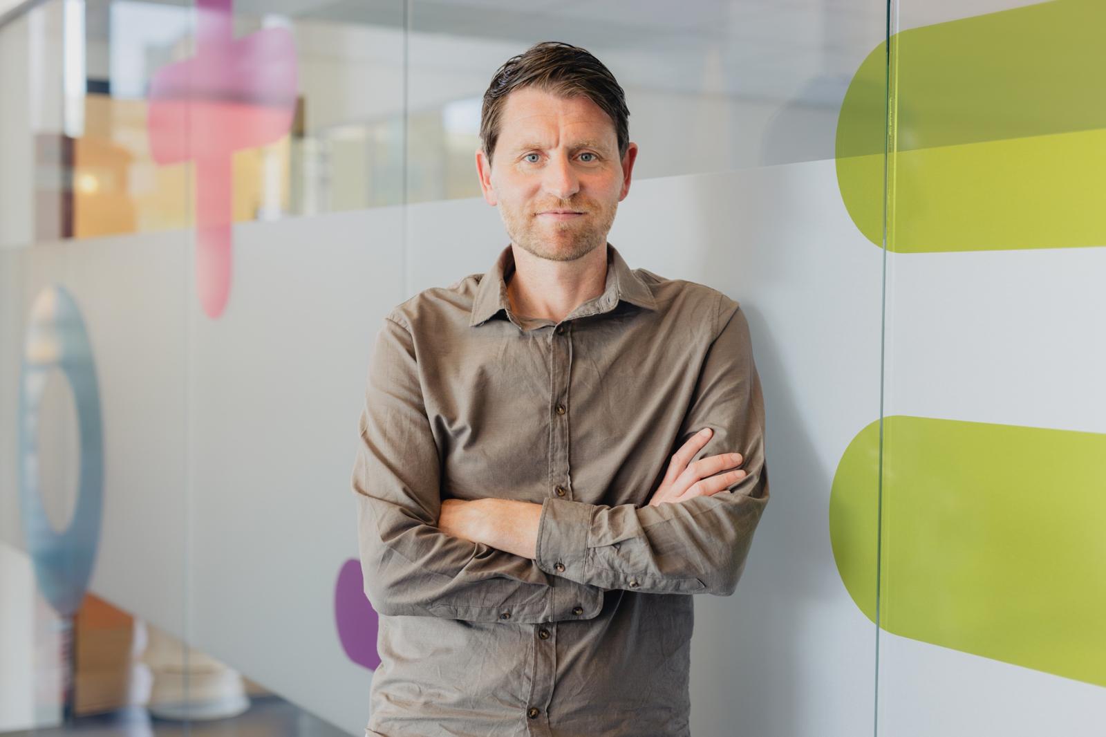 Woordvoerder van Noorderpoort staat met armen gekruist in een lichte kantooromgeving.