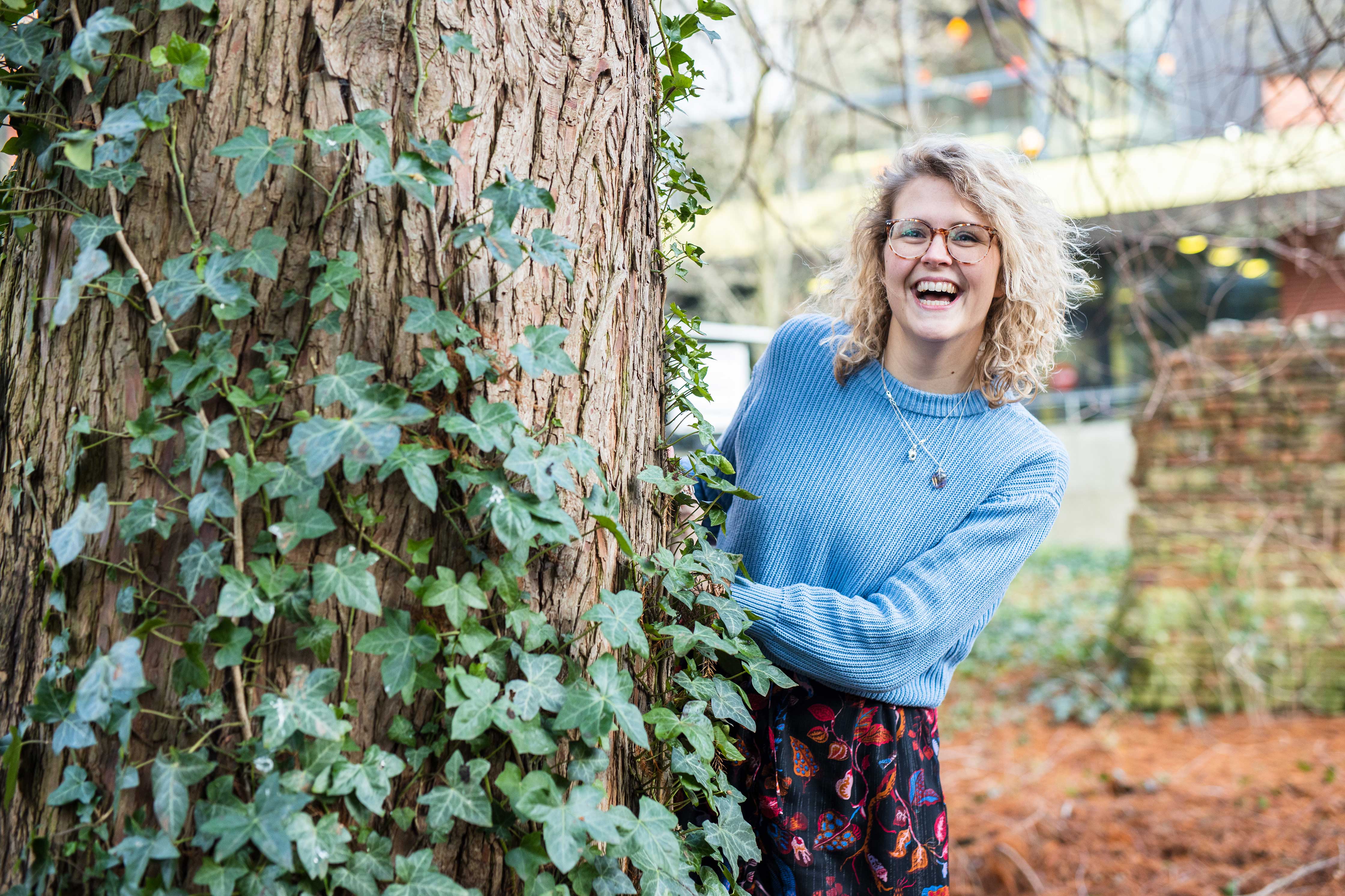 Persoon die buiten lacht achter een boom met klimop, passend bij duurzame thema's van Noorderpoort