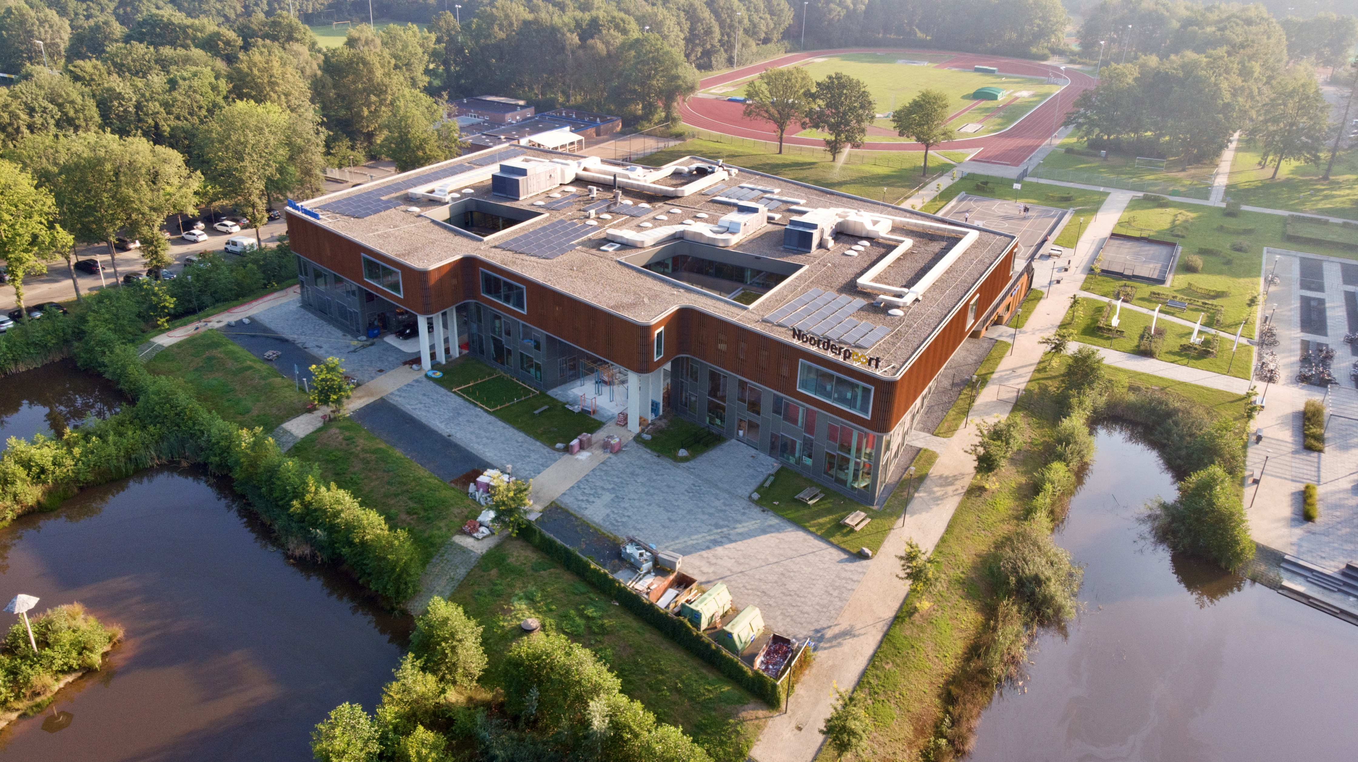 Luchtfoto van het onderwijsgebouw aan Sportparklaan 5 in Stadskanaal met rondom water en een sportveld.