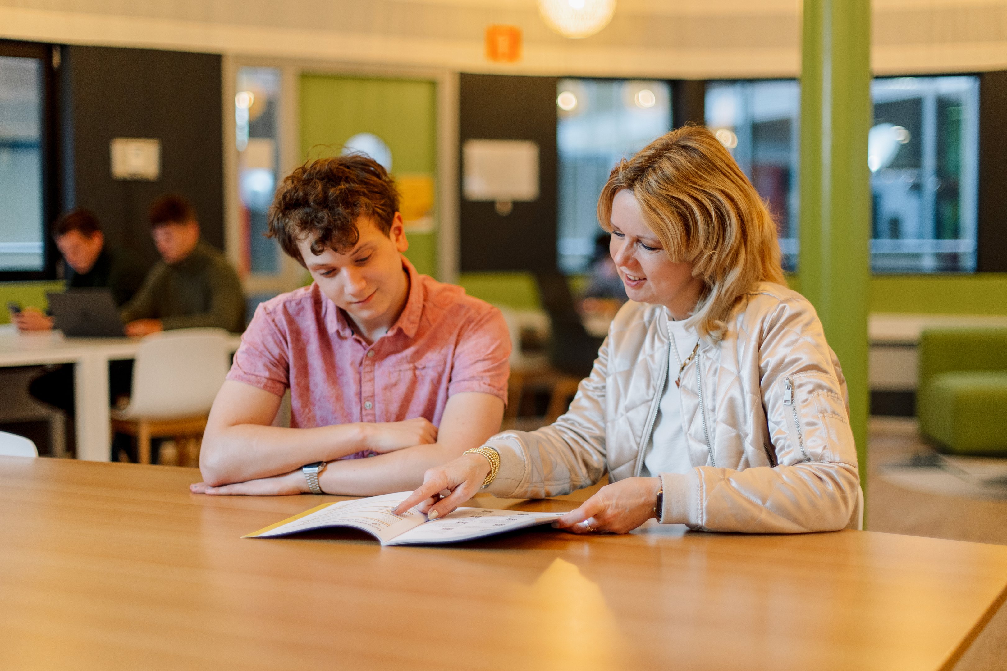 Begeleider bespreekt leerstof met een student aan tafel, gericht op studieondersteuning en groei.