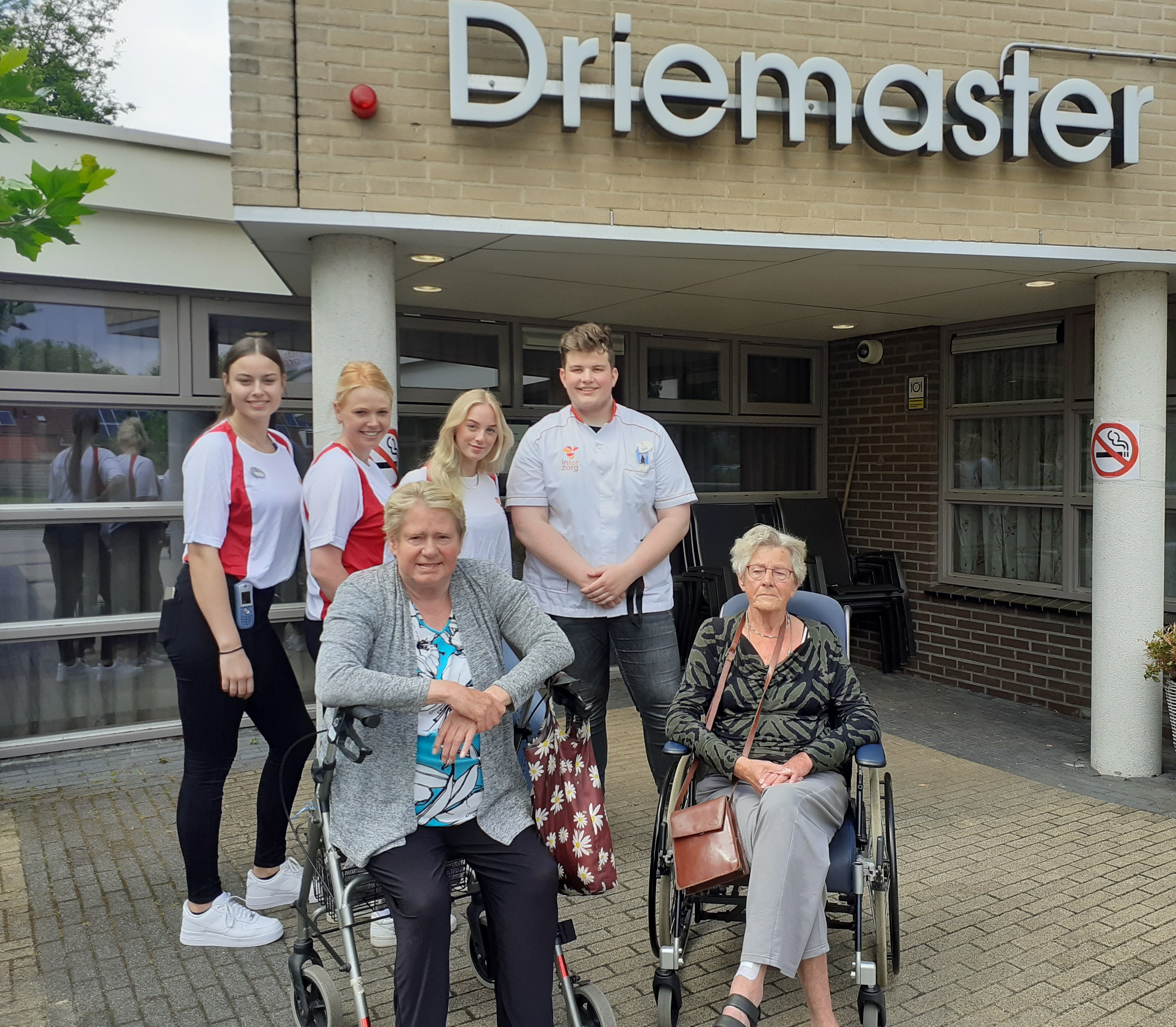 Studerende en cliënten staan en zitten samen voor het gebouw De Driemaster, locatie van Noorderpoort in Noord-Nederland.