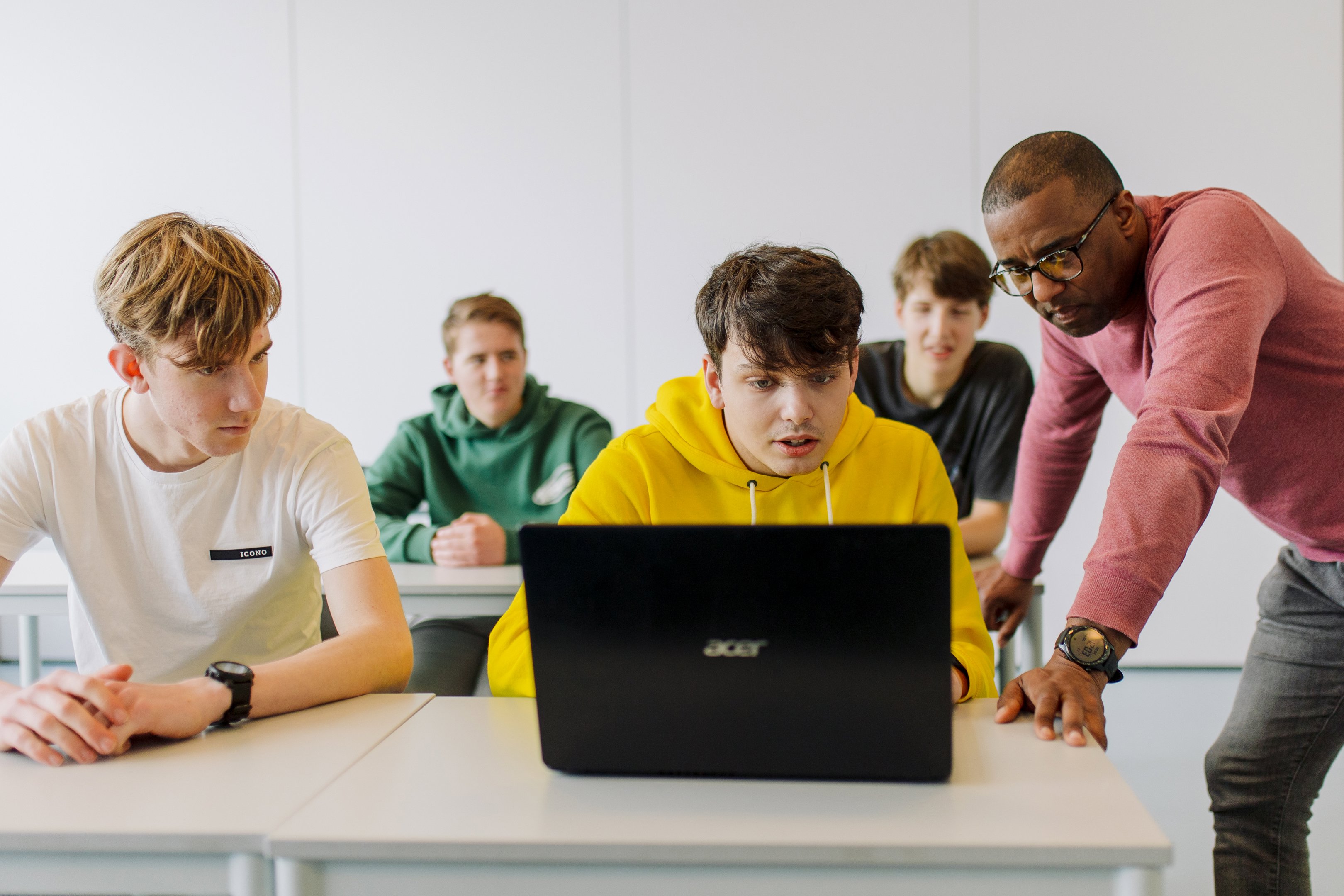 Docent begeleidt groep studenten tijdens interactieve les met laptop aan tafel in klaslokaal